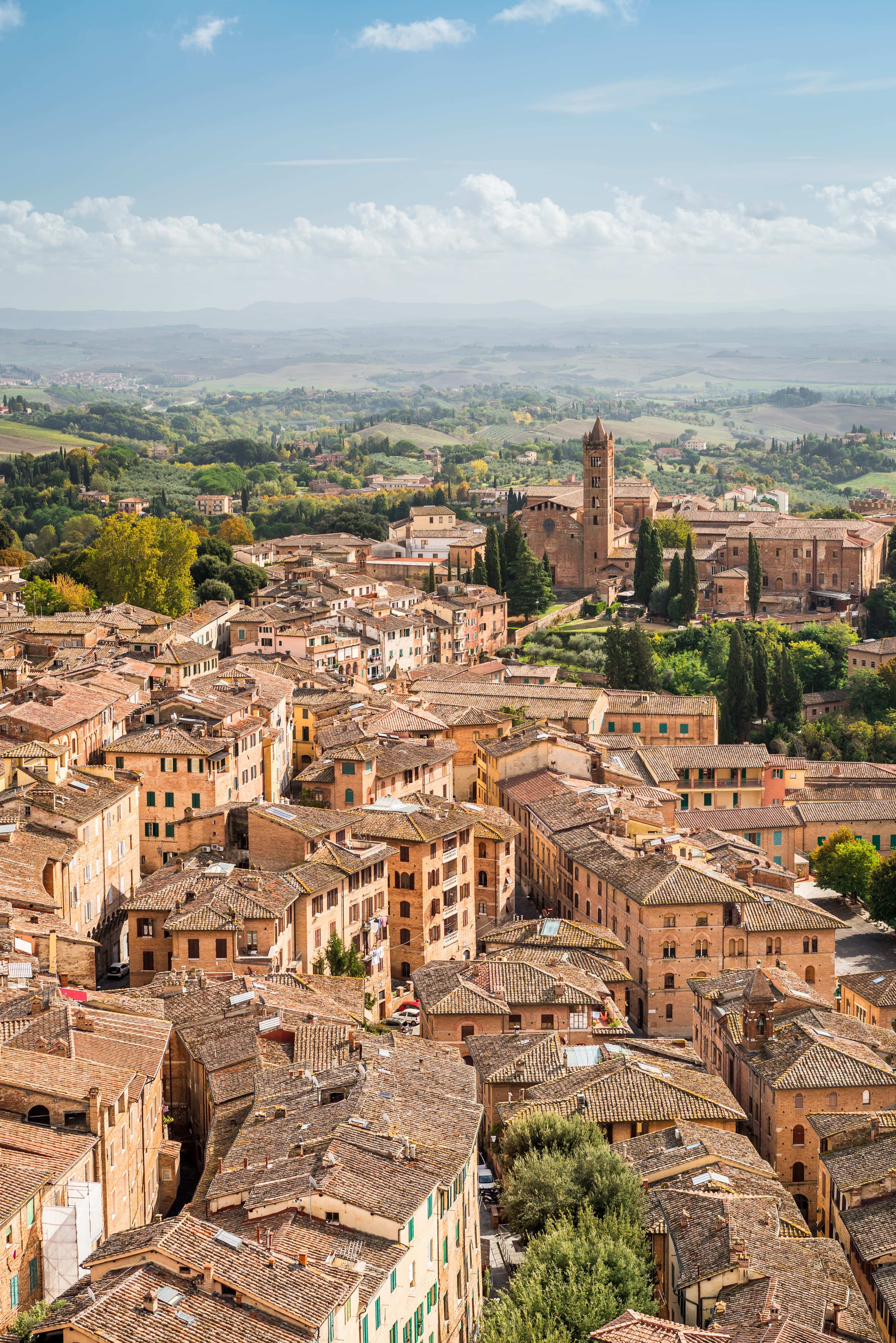 The tan and orange colorful town of Lucca with green trees immersed throughout in Tuscany, Italy.