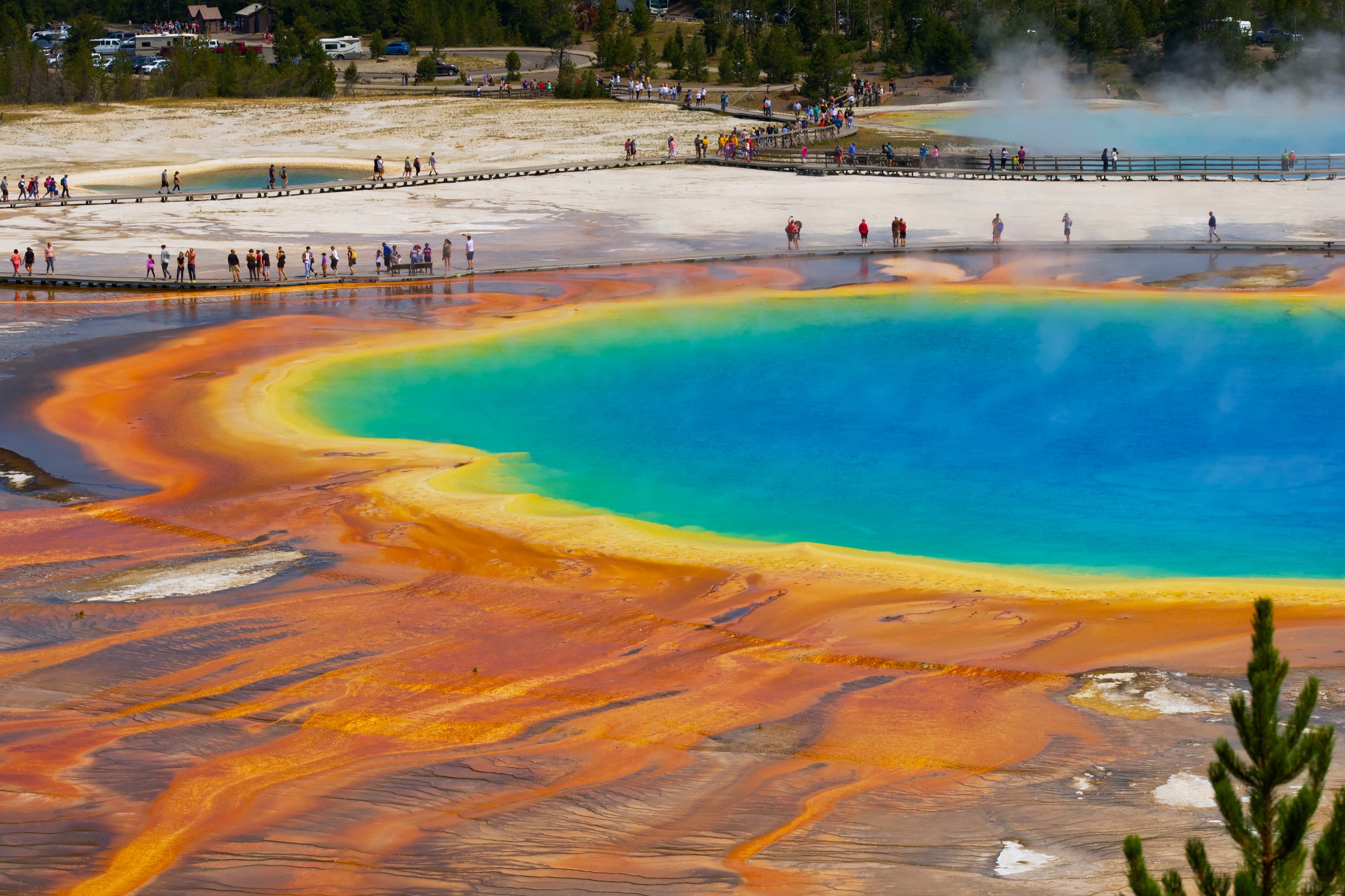 An orange, yellow, green and blue geysir in Yellowstone National Park with people standing around the outskirts.