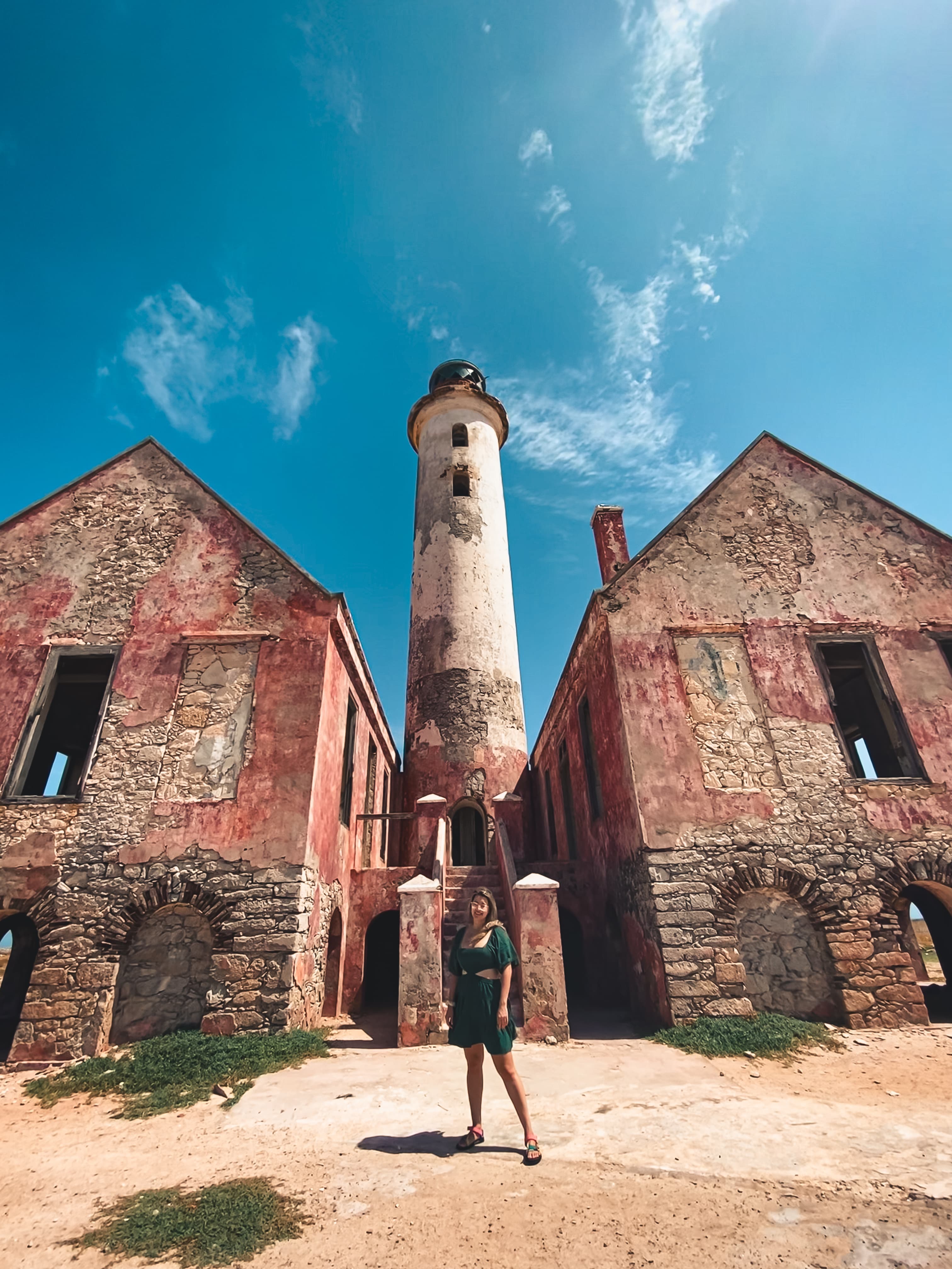 A woman standing on a dirt road in front of two old buildings and a stone tower.