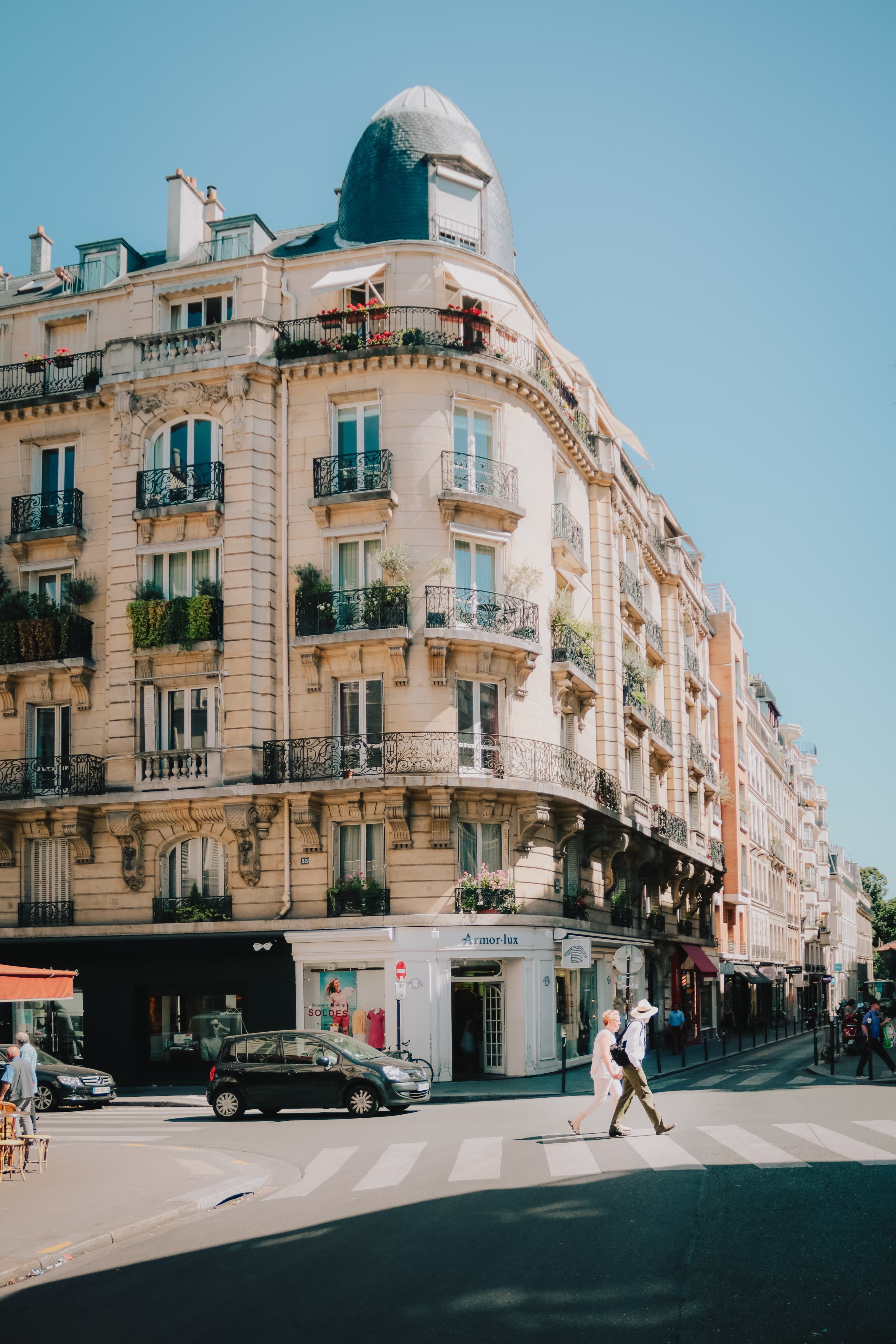 Two people walking on the street next to a tall building on a sunny day