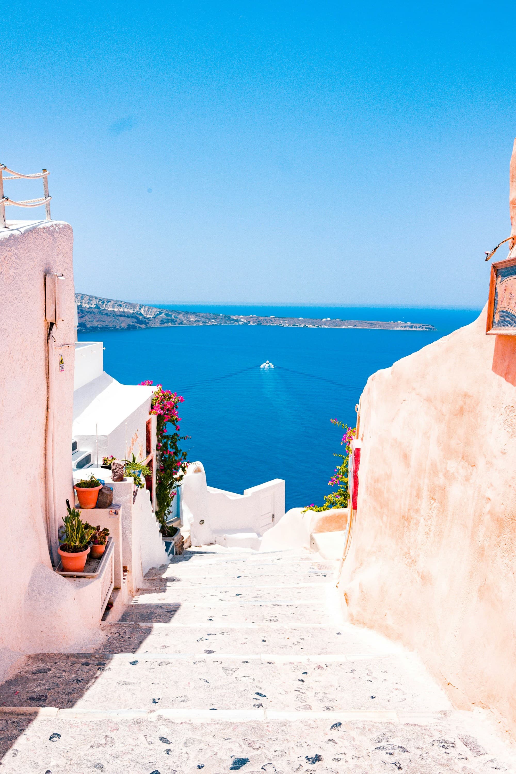 Pink stairs going down with view of ocean with a boat.