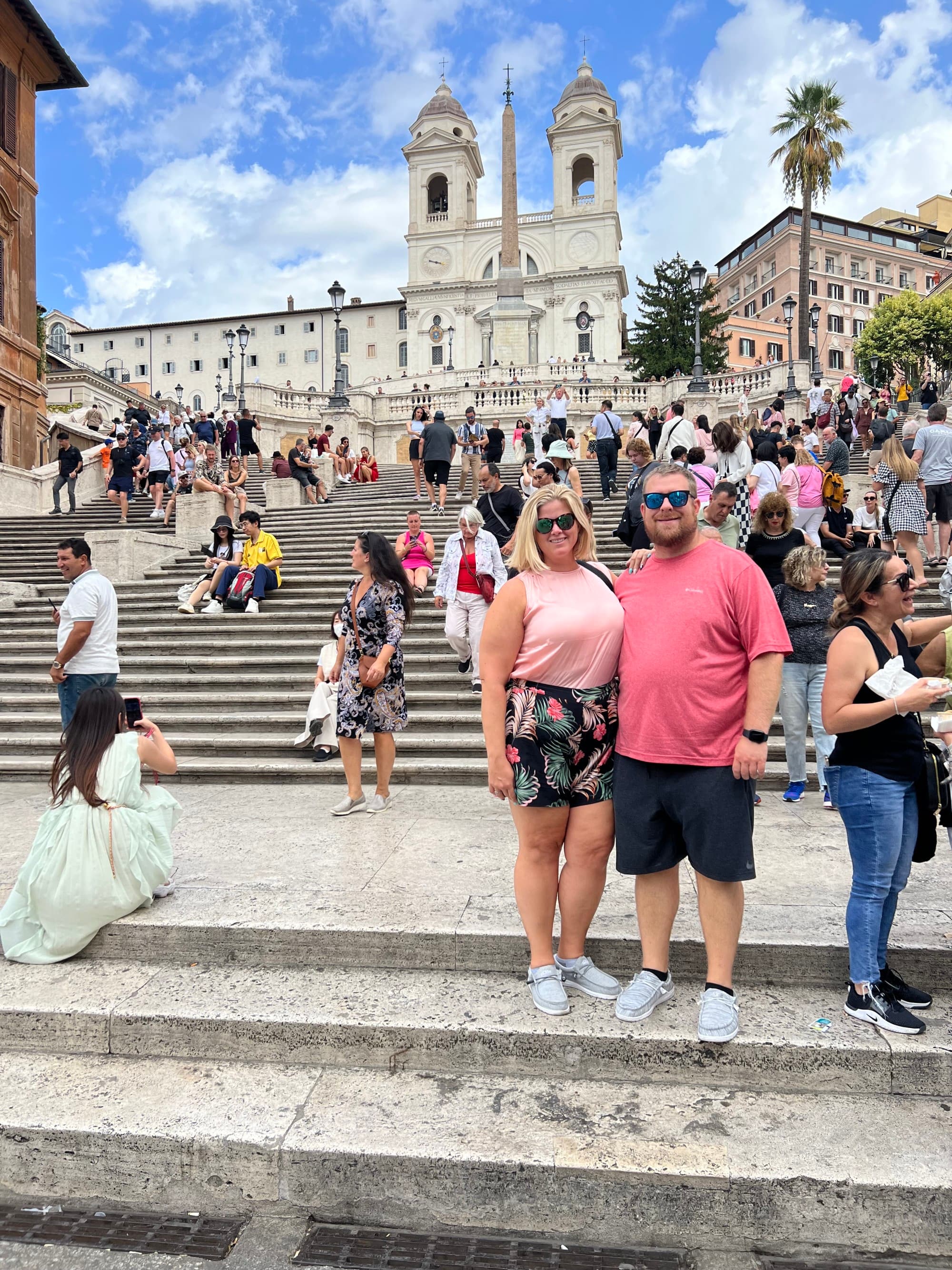 A picture of a couple with many people in the background, standing in front of an ancient Roman building.