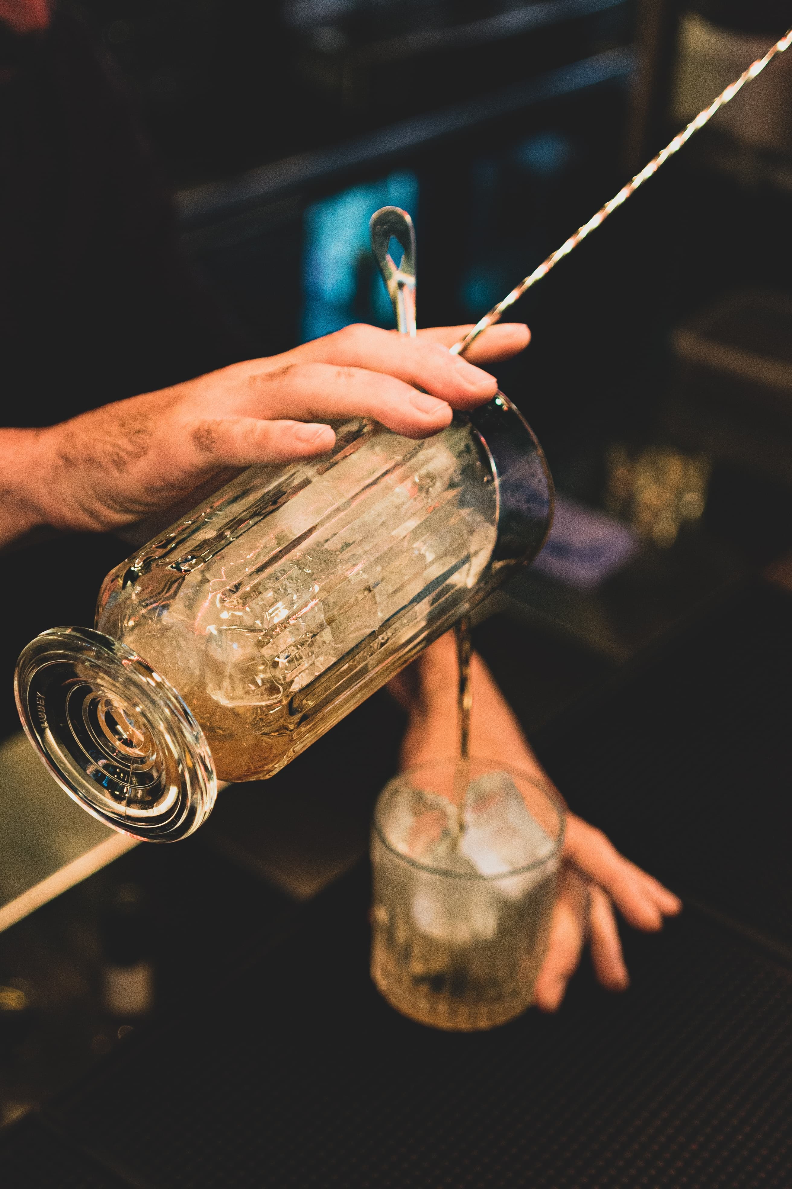 A bartender making a drink and pouring into cup.