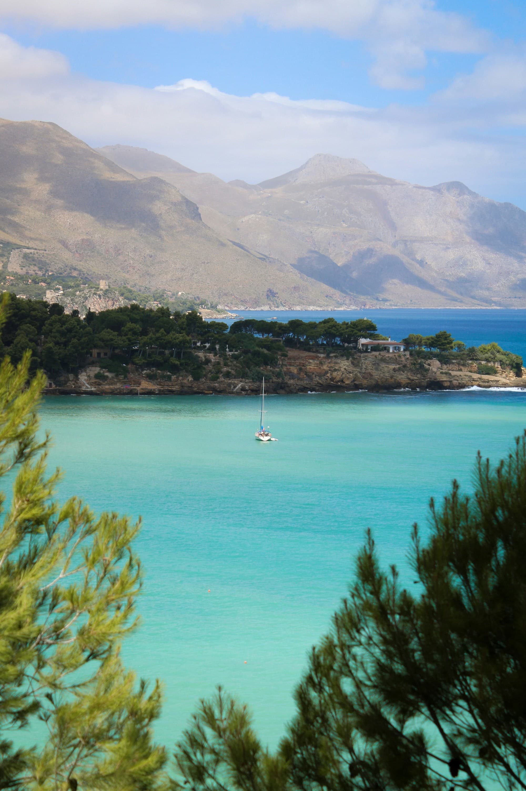 Sailboat off the coast with rocky outcroppings at daytime.