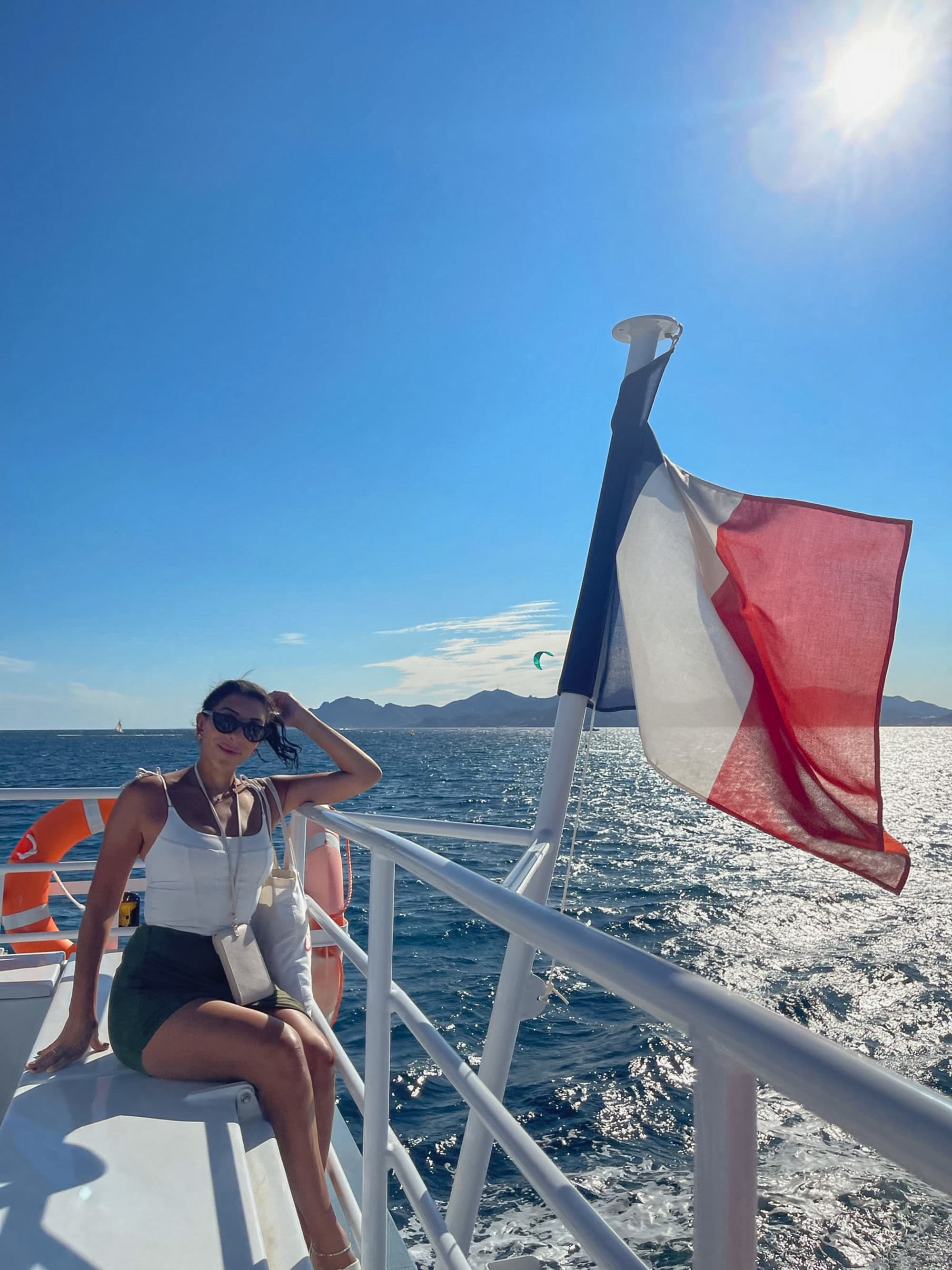 A girl sitting on a yacht with a flag next to her during the daytime.