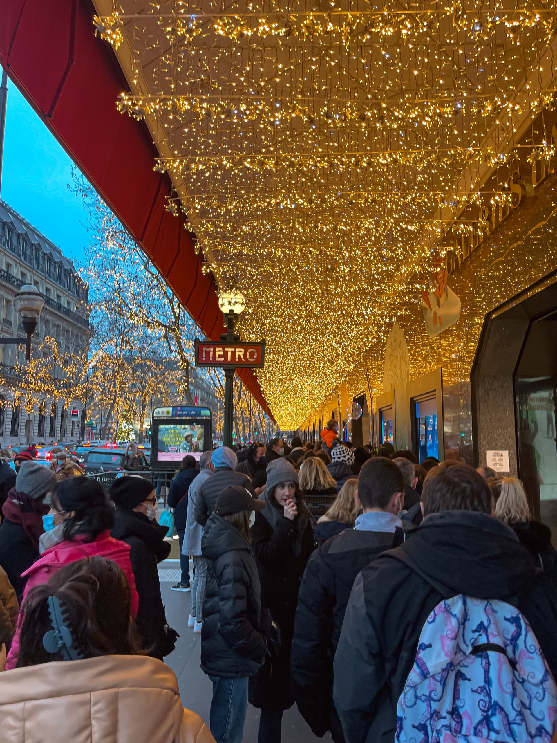 People standing on side of streets covered with lights.