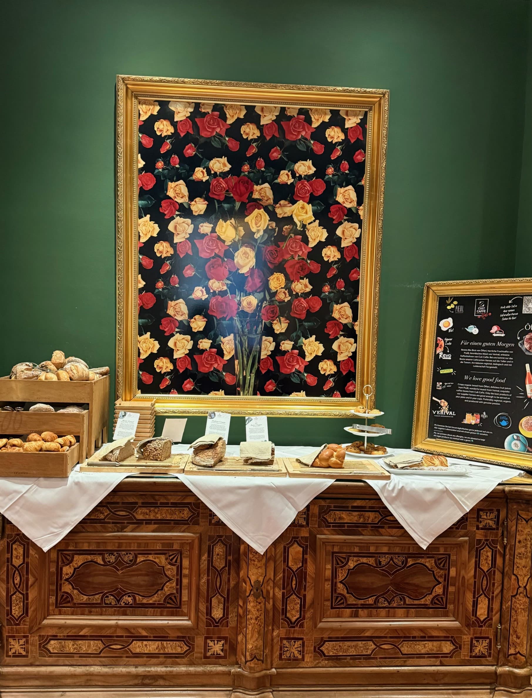 A display of food and pastries on a wooden dresser against a green-painted wall and a piece of artwork above