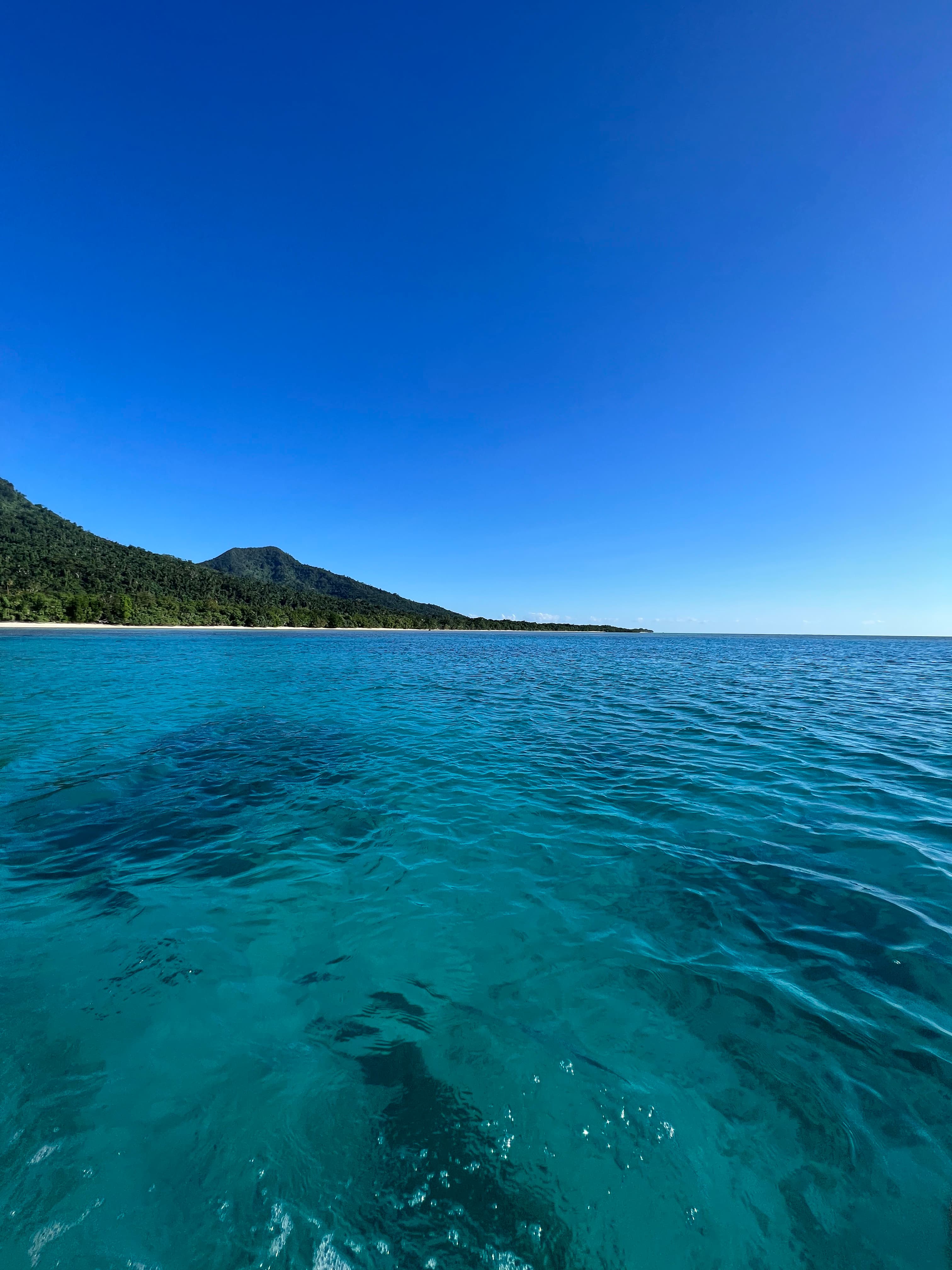 Clear blue waters and a small hill on a beach seen from a boat.