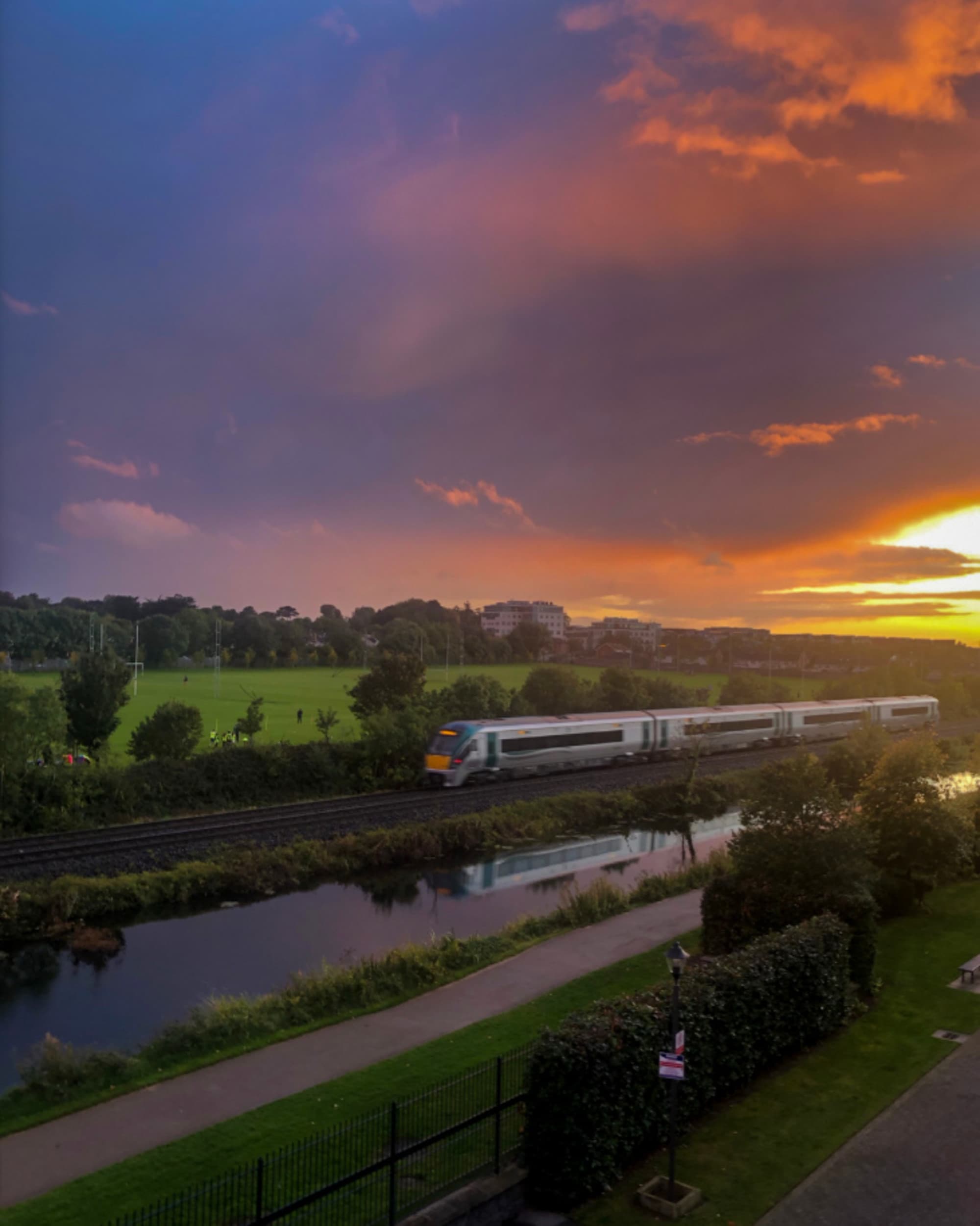 A scenic sunset with vibrant clouds reflected over a body of water, alongside a train on adjacent tracks, as seen on a trip through Ireland by train.