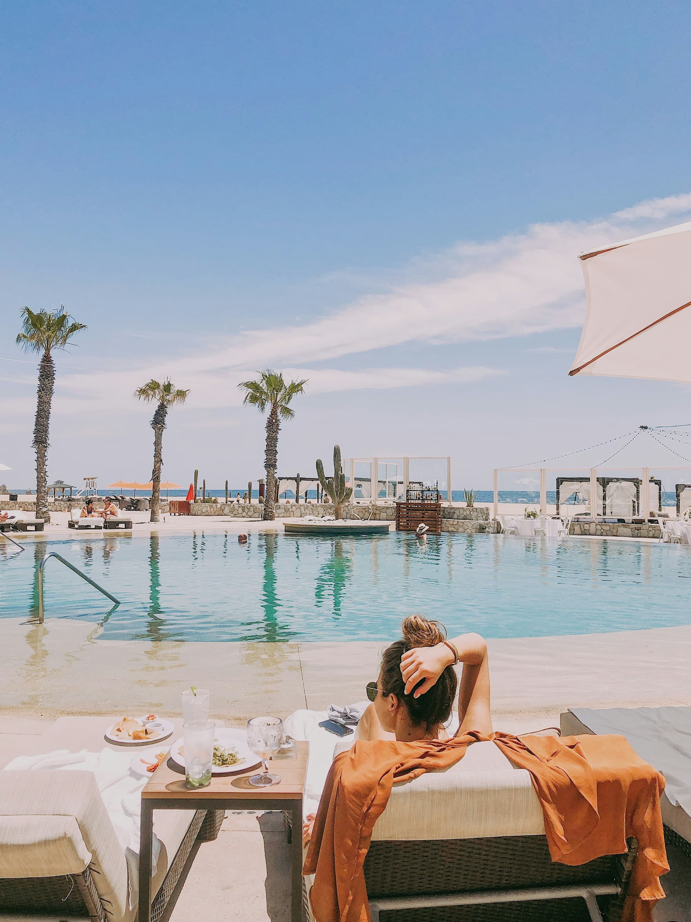 A woman lying on a lounge chair next to a pool area during the daytime