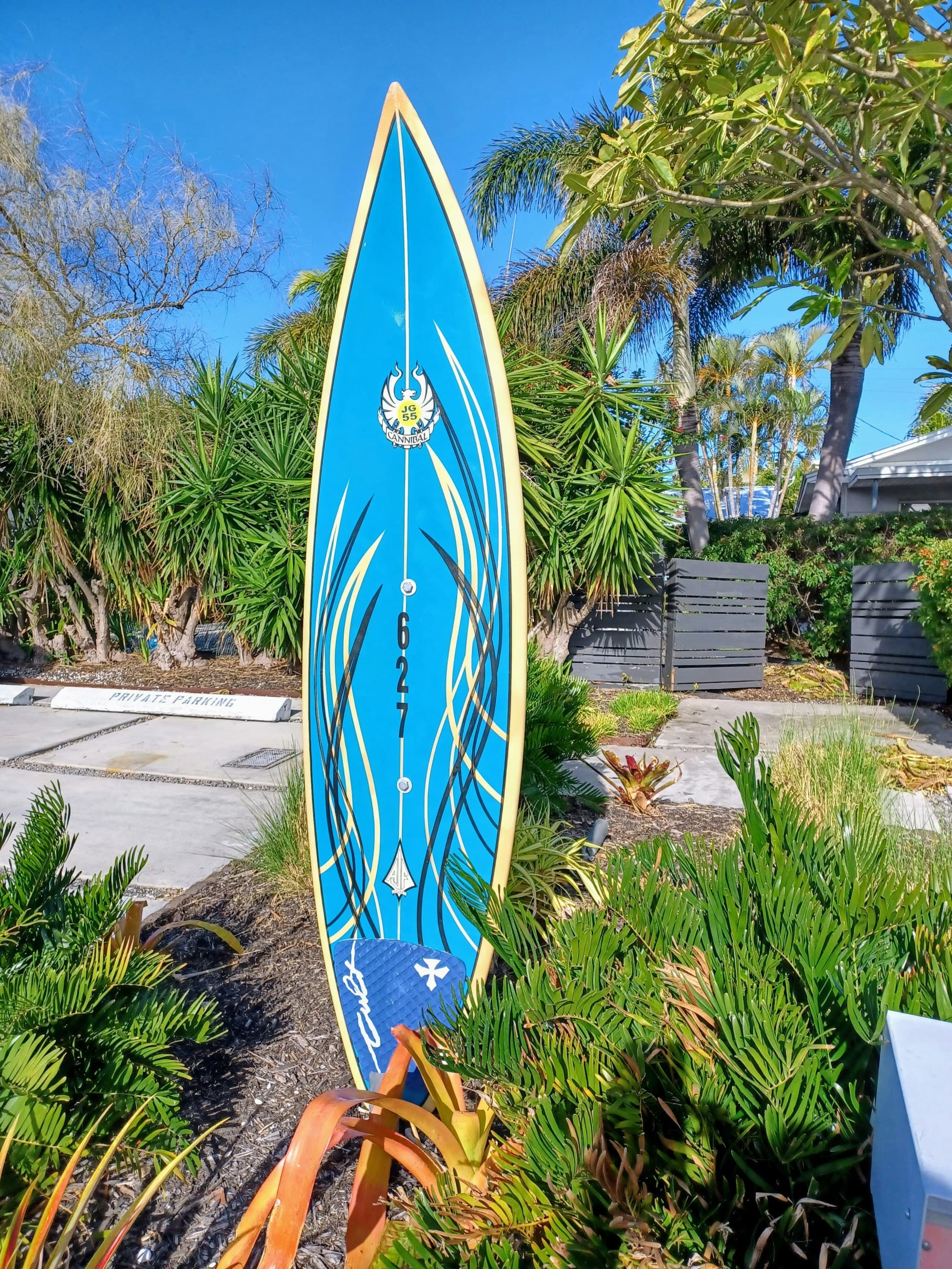 A blue surfboard standing up in an outdoor garden during the daytime