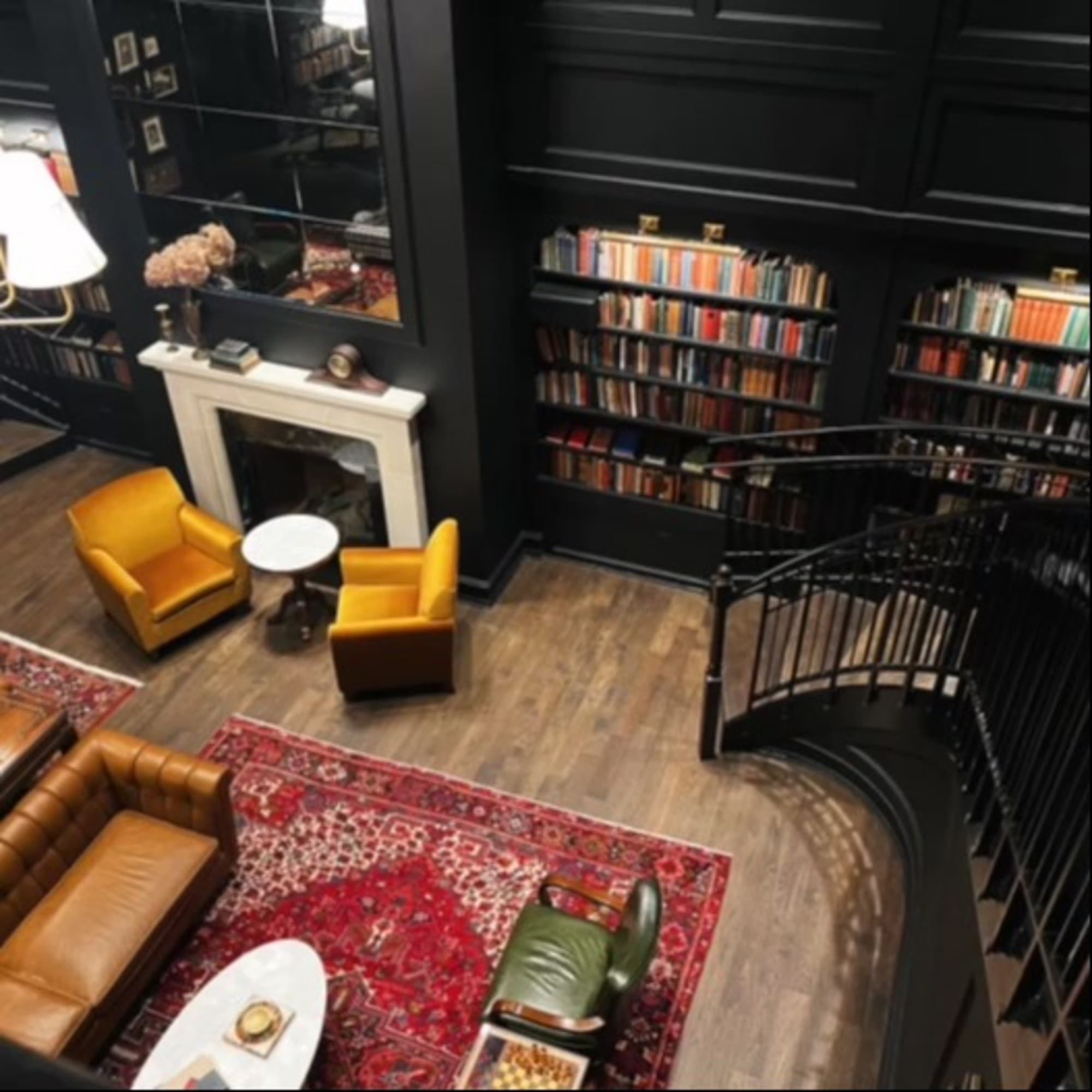 A dimly-lit room with tall book cases and lots of seating, photo taken for the top of a staircase