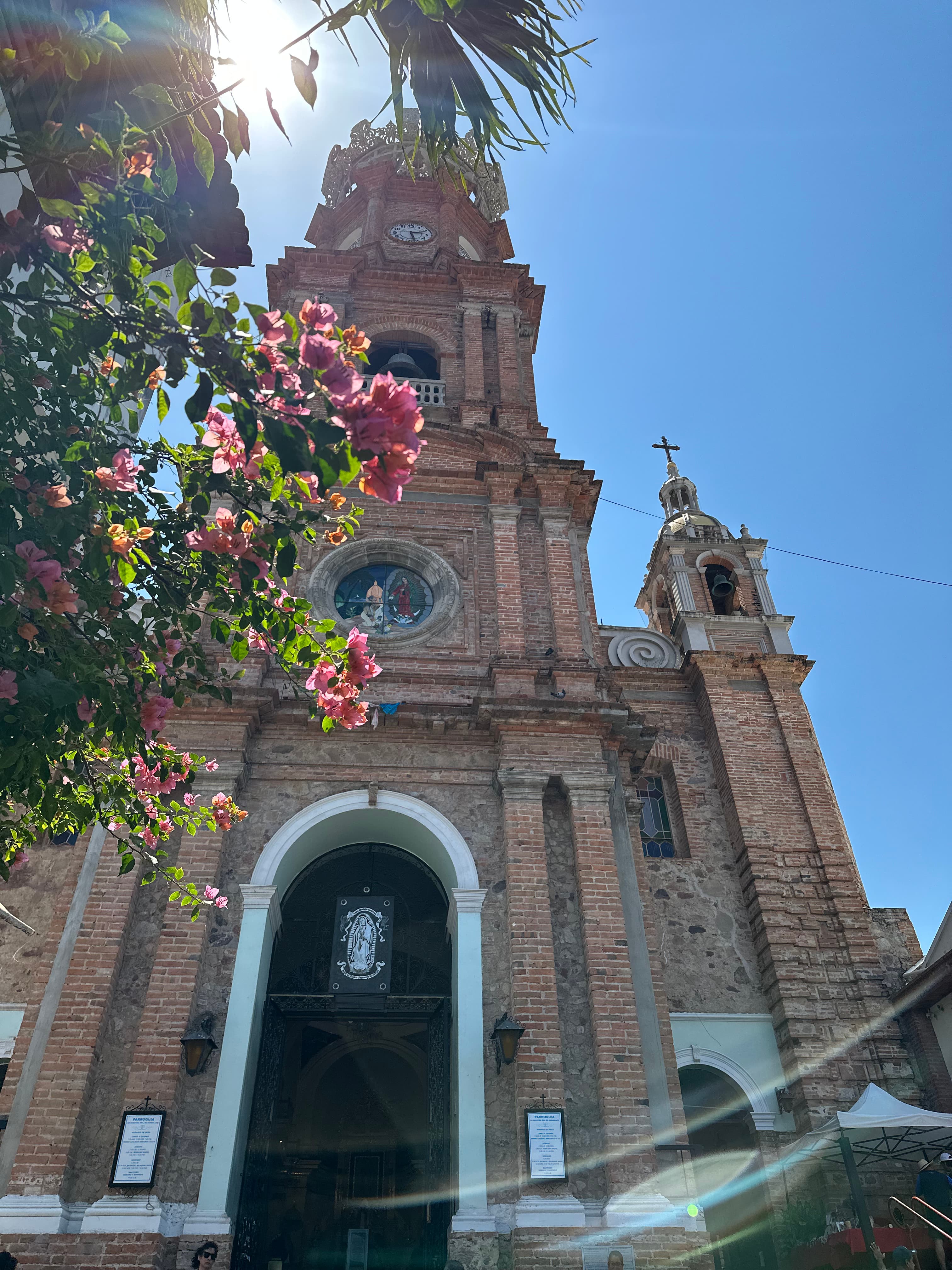 A below angle taken of the exterior of a stone Church, with leaves and flowers of a tree in sight.