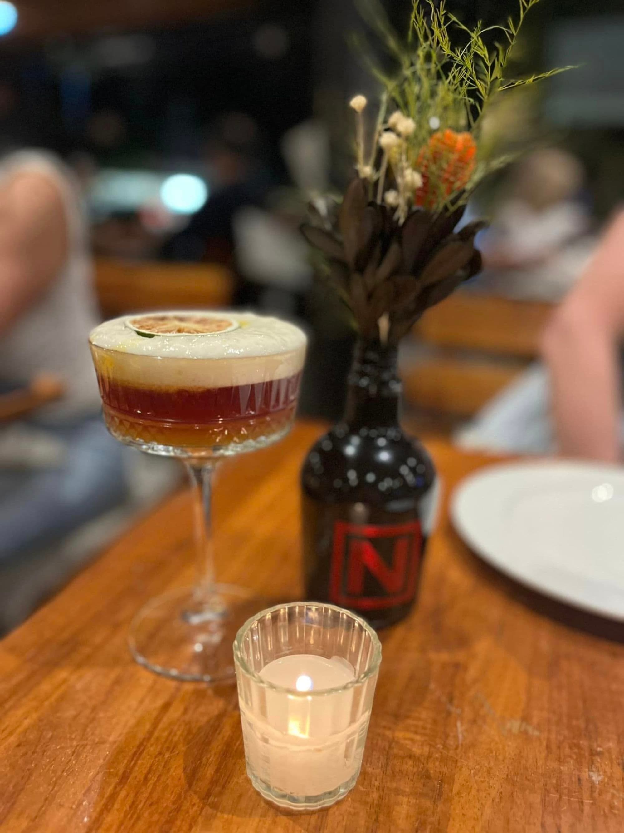 A sophisticated bar scene featuring a layered cocktail, fresh flowers, and the warm glow of candlelight.