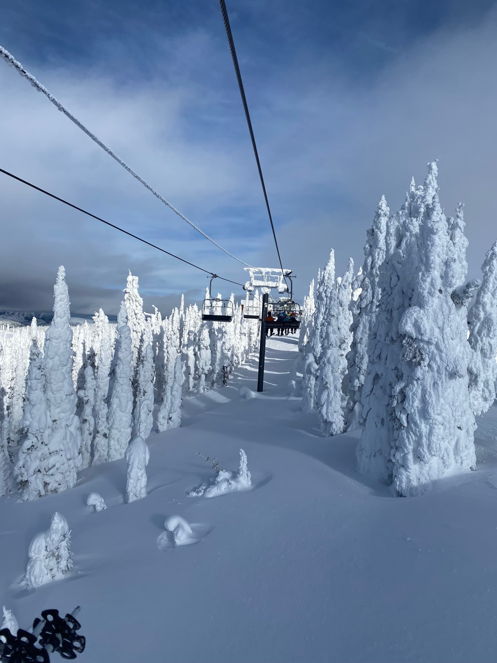 A view of snowy terrain and snow covered trees from a ski lift.