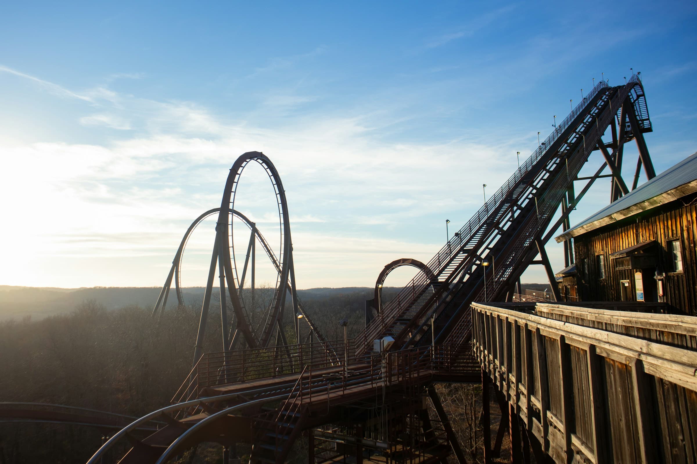 A view of amusement park rides with a vast blue sky in the background. The sun is also shining towards the left of the photo.