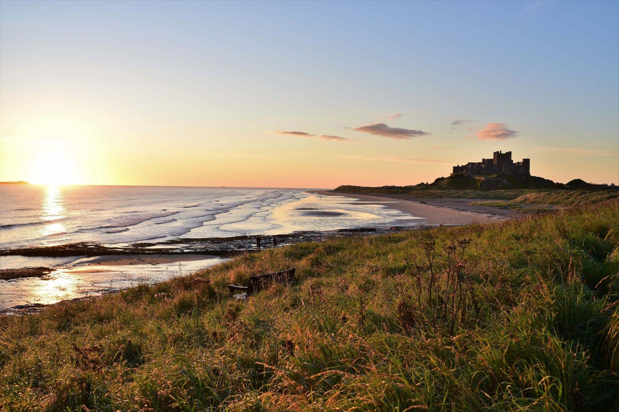 A beach with green field and a castle at the back.