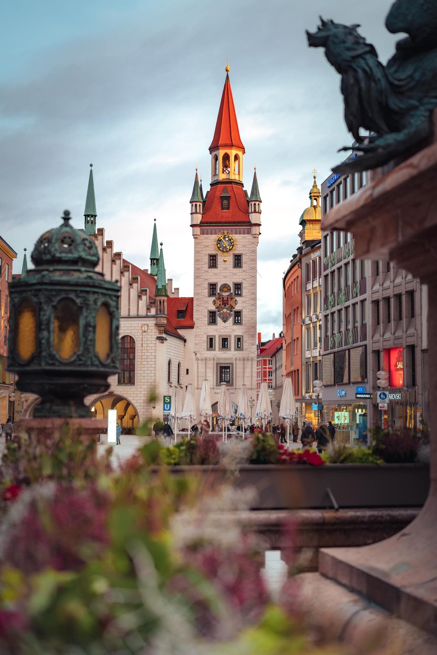 View of iconic tower in Munich from fountain on bright but cloudy day.