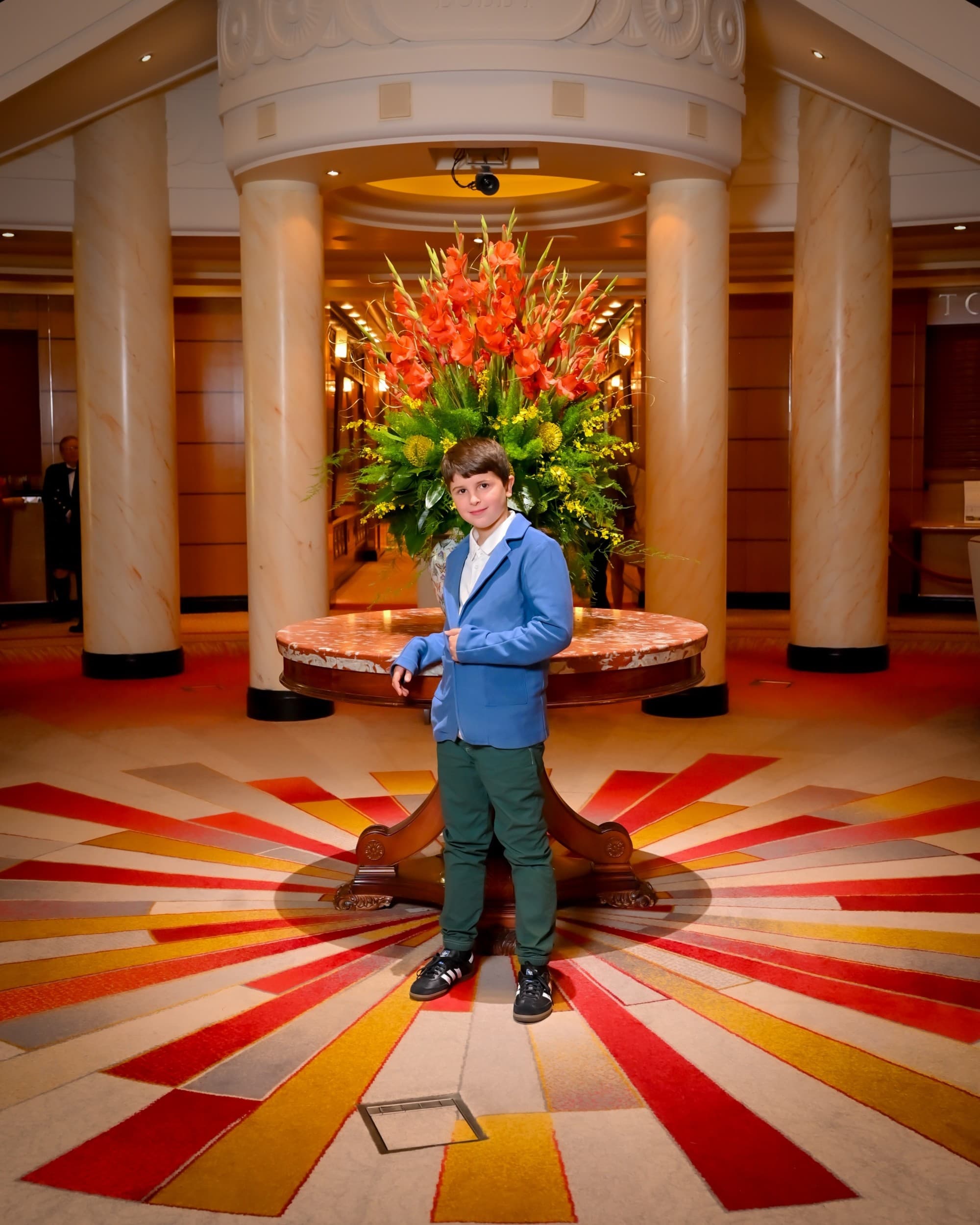 A kid posing in a sport jacket in front of a table with a floral arrangement.