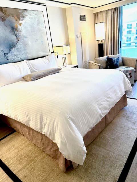 King-sized bed with fluffy white linens and an abstract painting overhead.