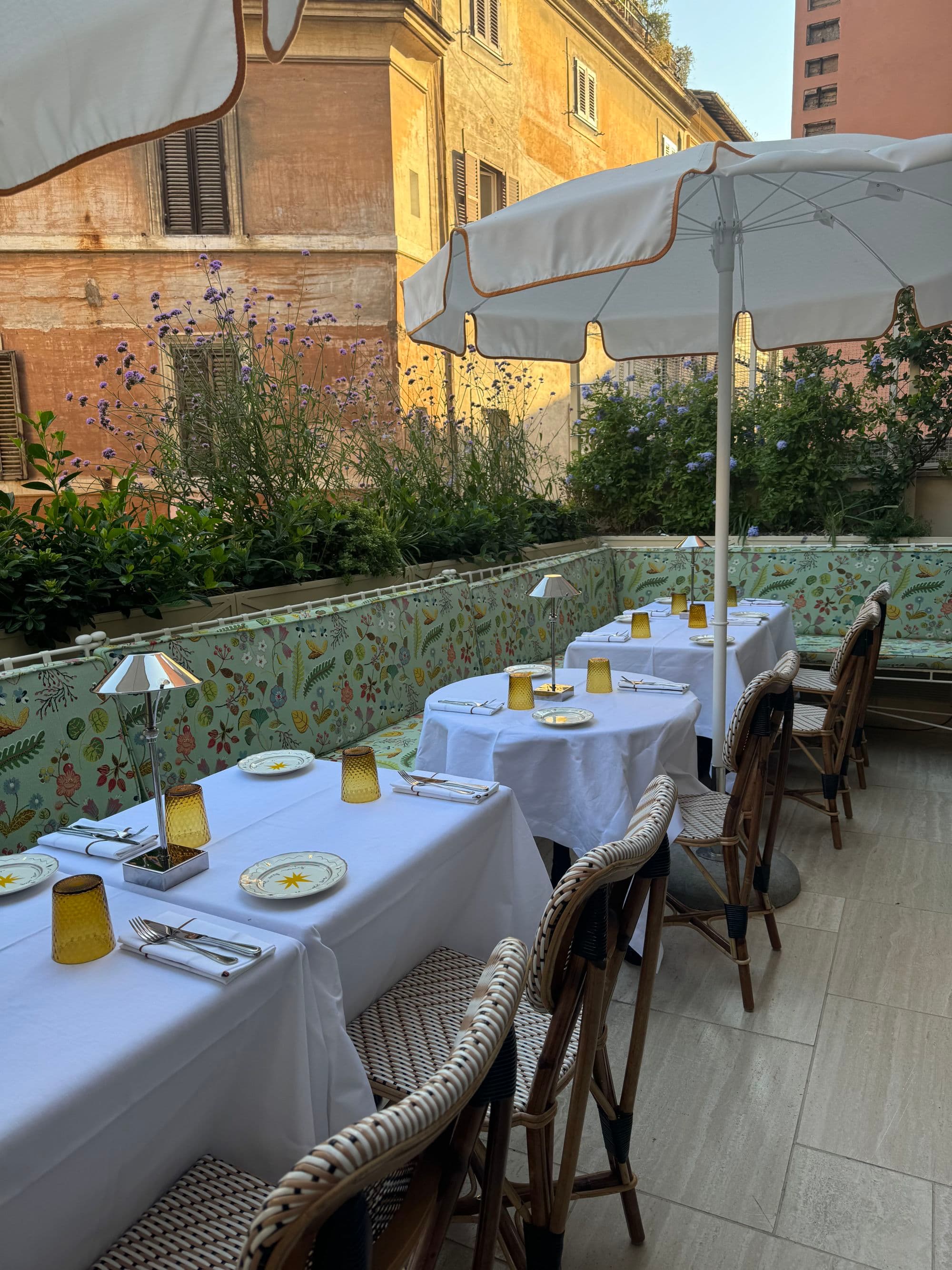 The outdoor hotel dining area is cheerful with floral pattern benches with beautiful flora growing beside the walled patio.