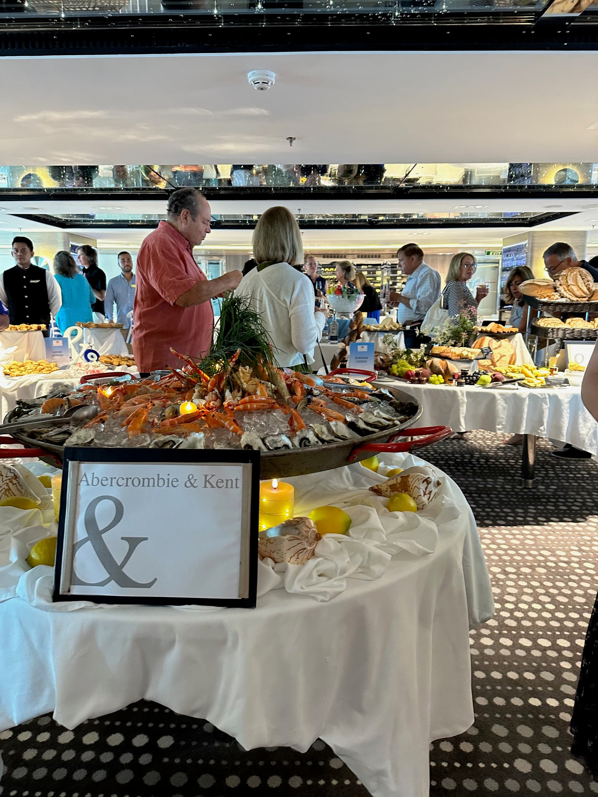 Tablecloth-lined tables set up with buffet food like crab legs and charcuterie on the ship - Kristyne Wada