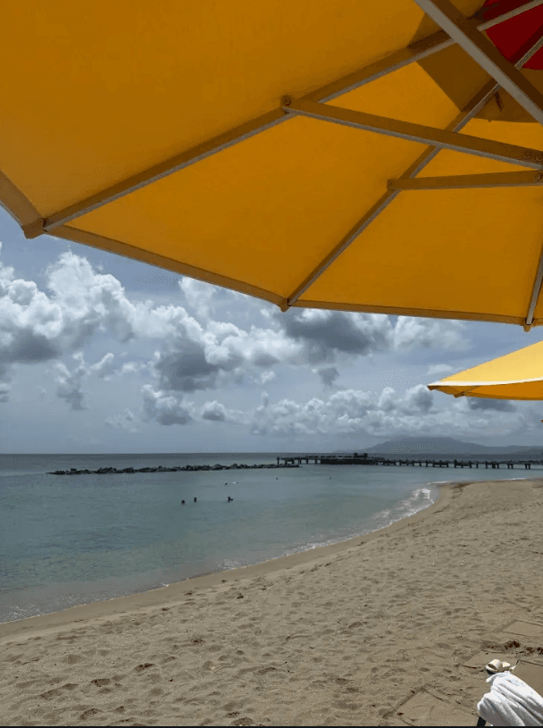 A view of the beach and waves from beneath a yellow umbrella on Pinney's Beach at Four Seasons Resort Nevis.