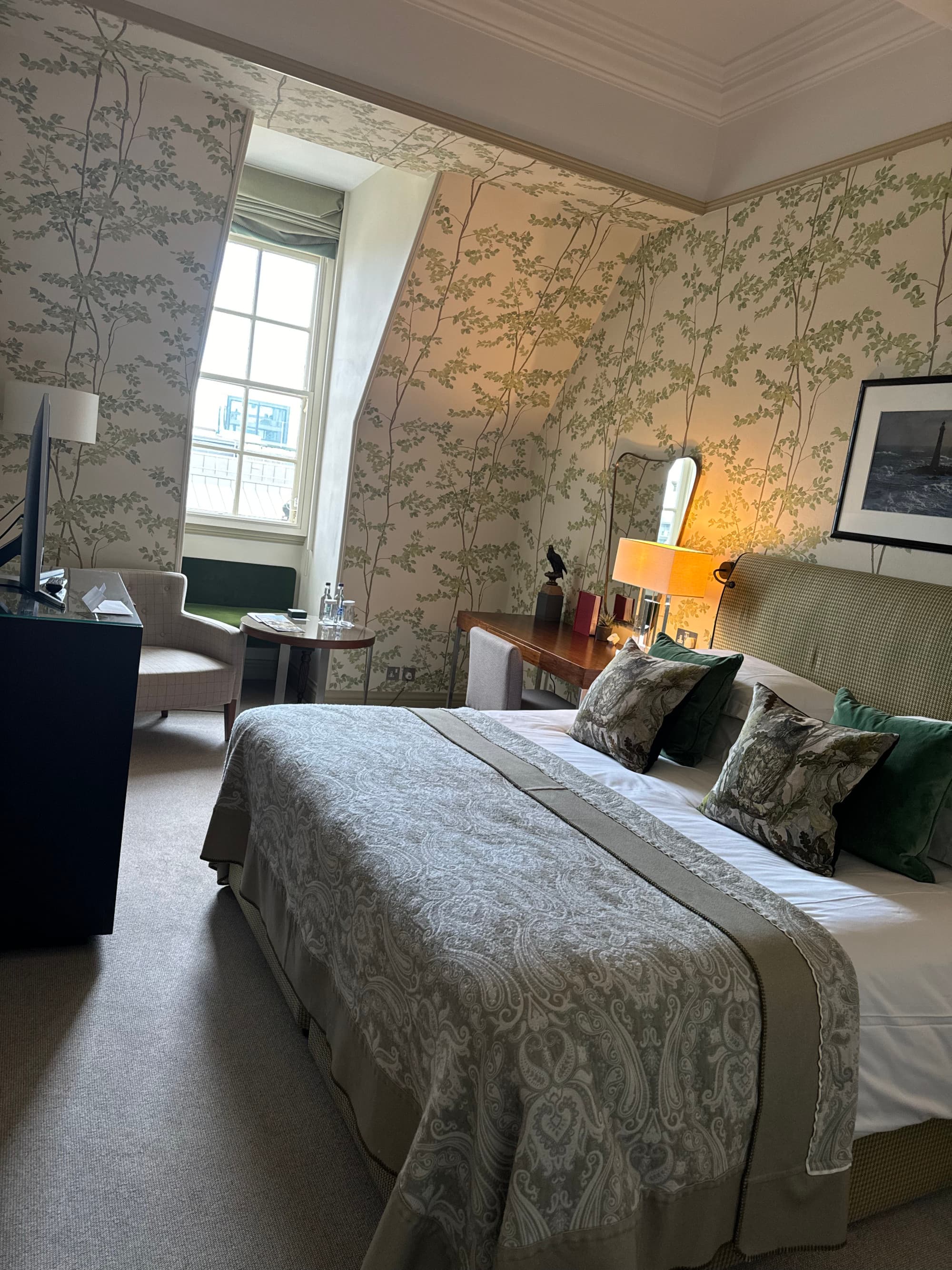 View of a bedroom at the Balmoral, with floral beige wallpaper, a bed and sitting area
