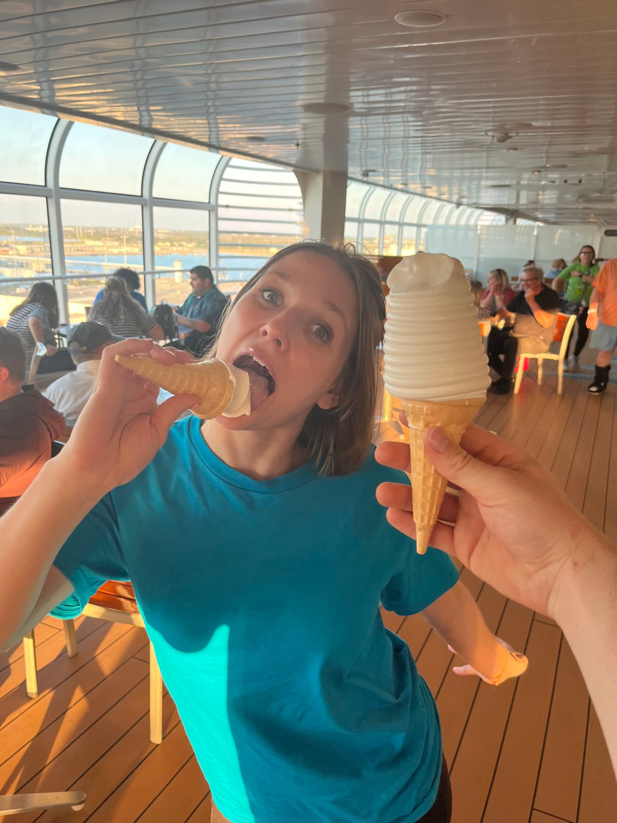 Travel advisor indulging in an ice cream cone, with someone holding another ice cream cone in front of her, with a view of the dining area in the background.