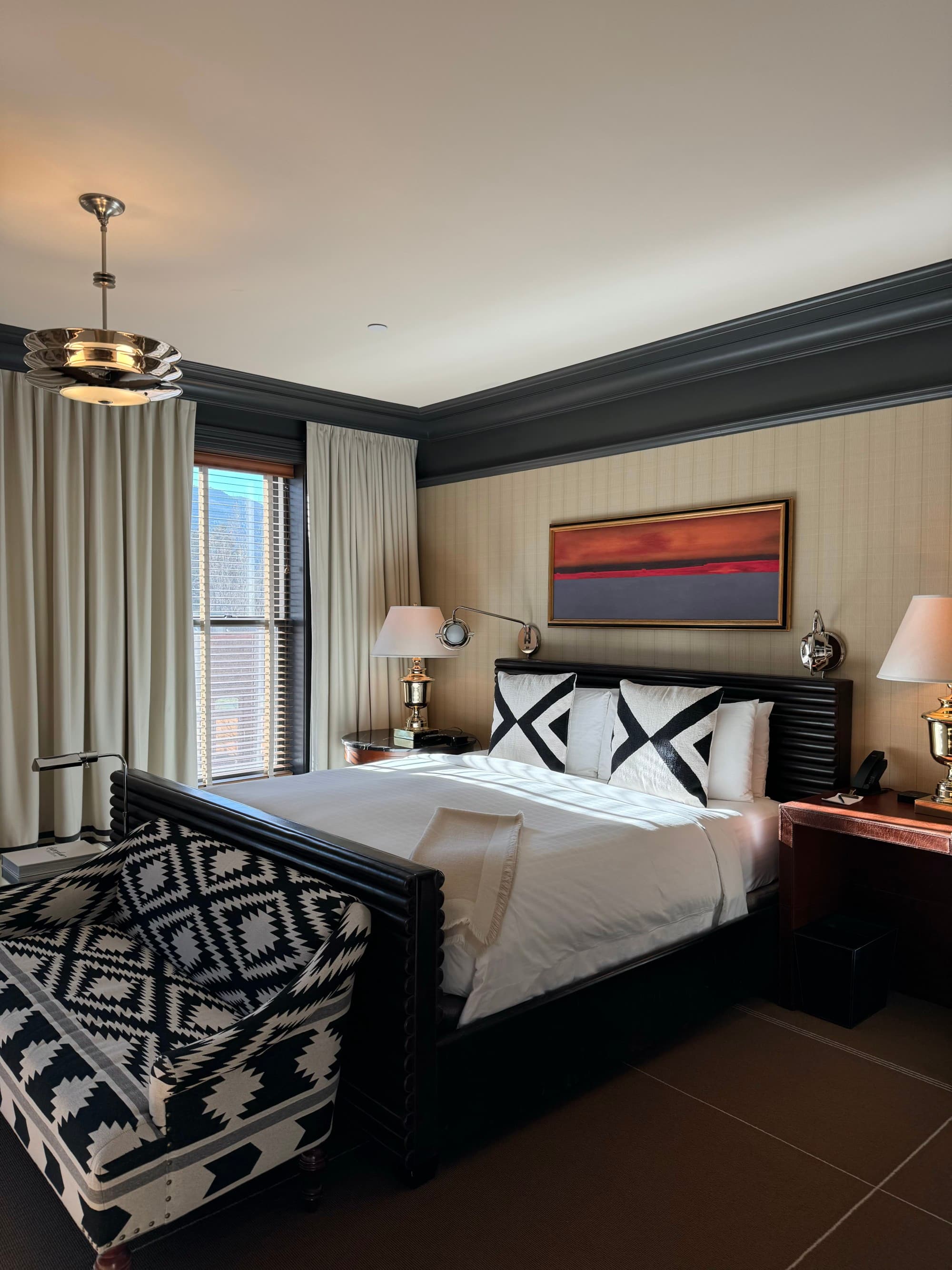Inside one of the hotel's bedrooms, white bed linens, artwork, floor-ceiling windows, and Native American patterns on the chair.