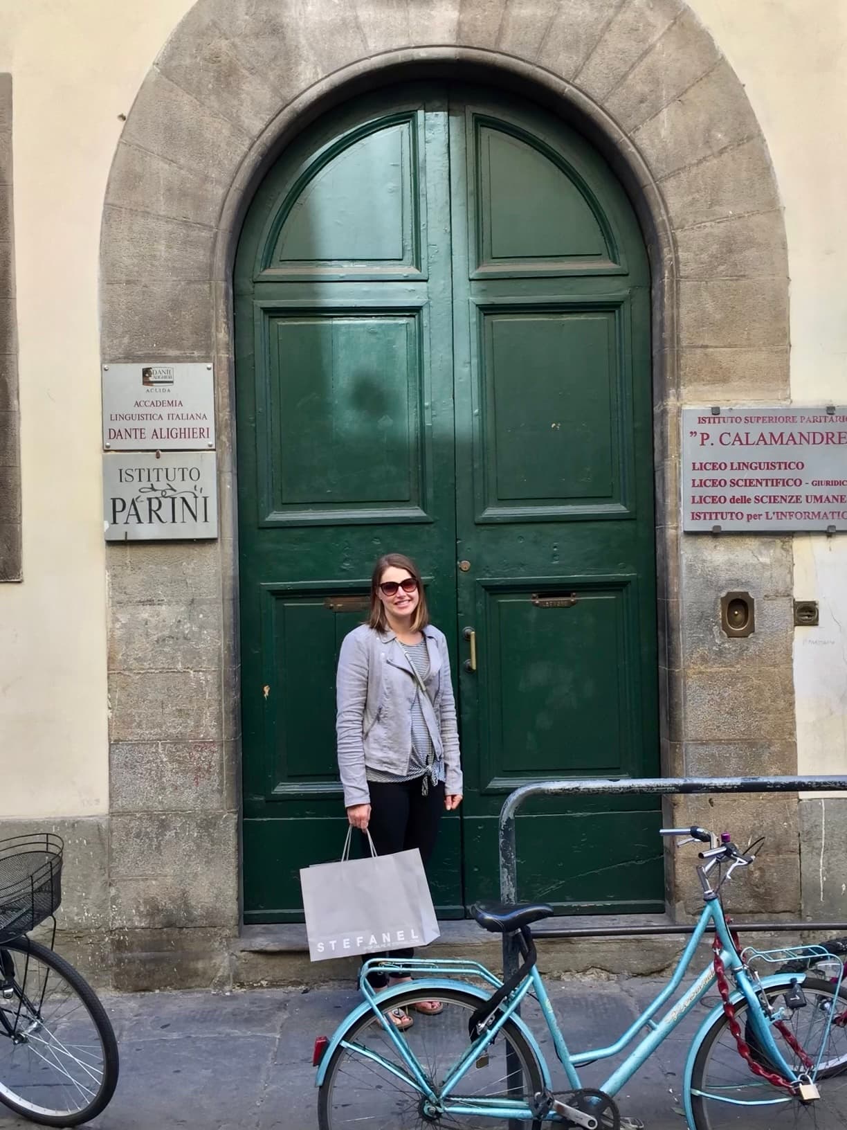 A woman holding a shopping bag stands in front of a green door