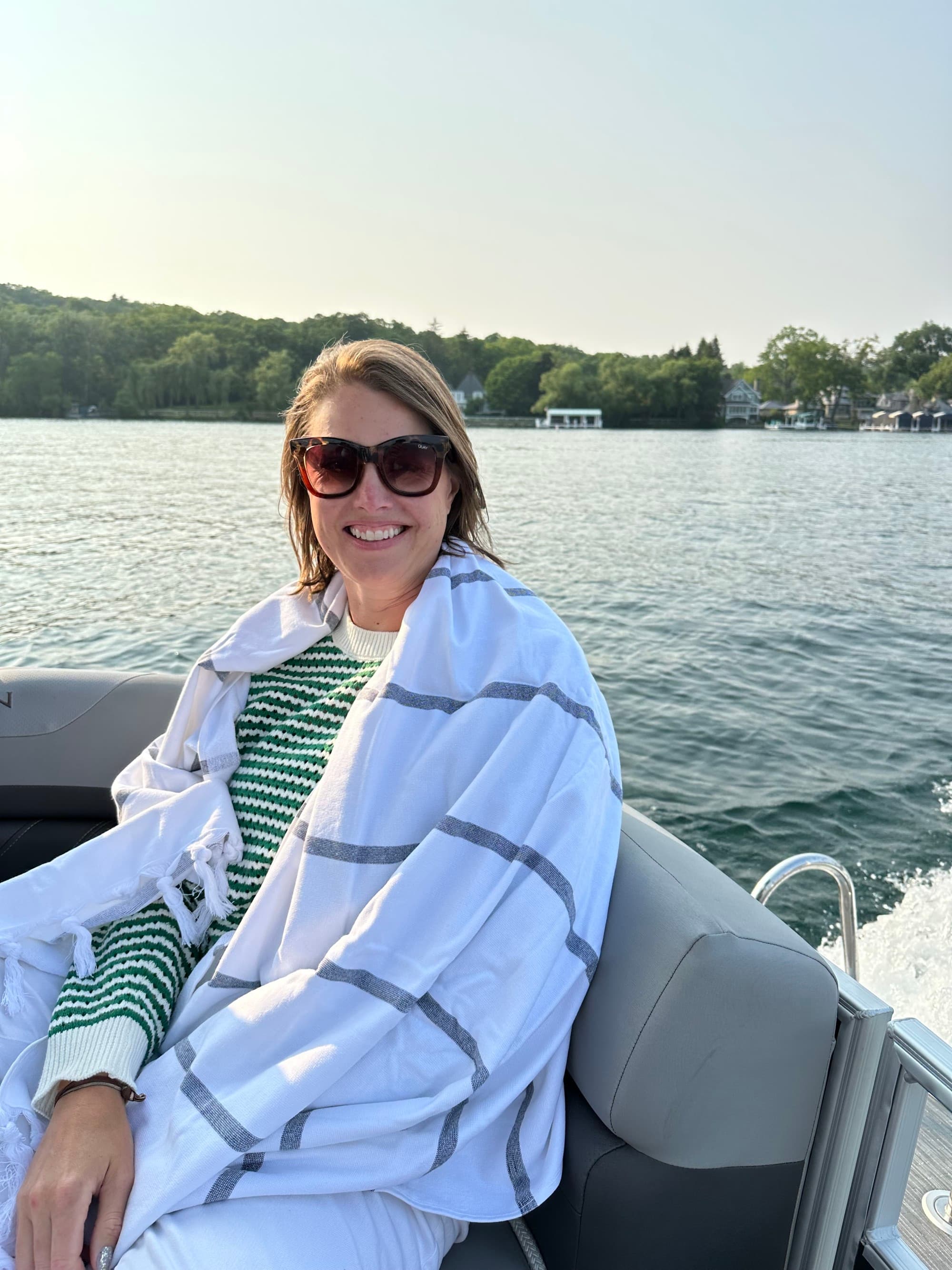 A woman wrapped in a white blanket and wearing sunglasses sits in a boat on a lake