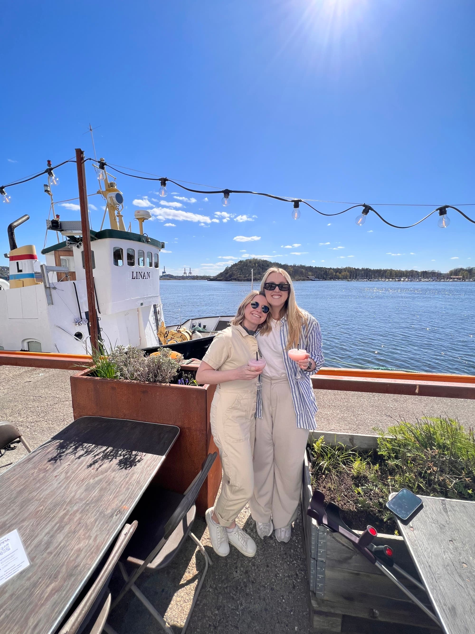 Two people posing on a pier in front a body of water during the daytime