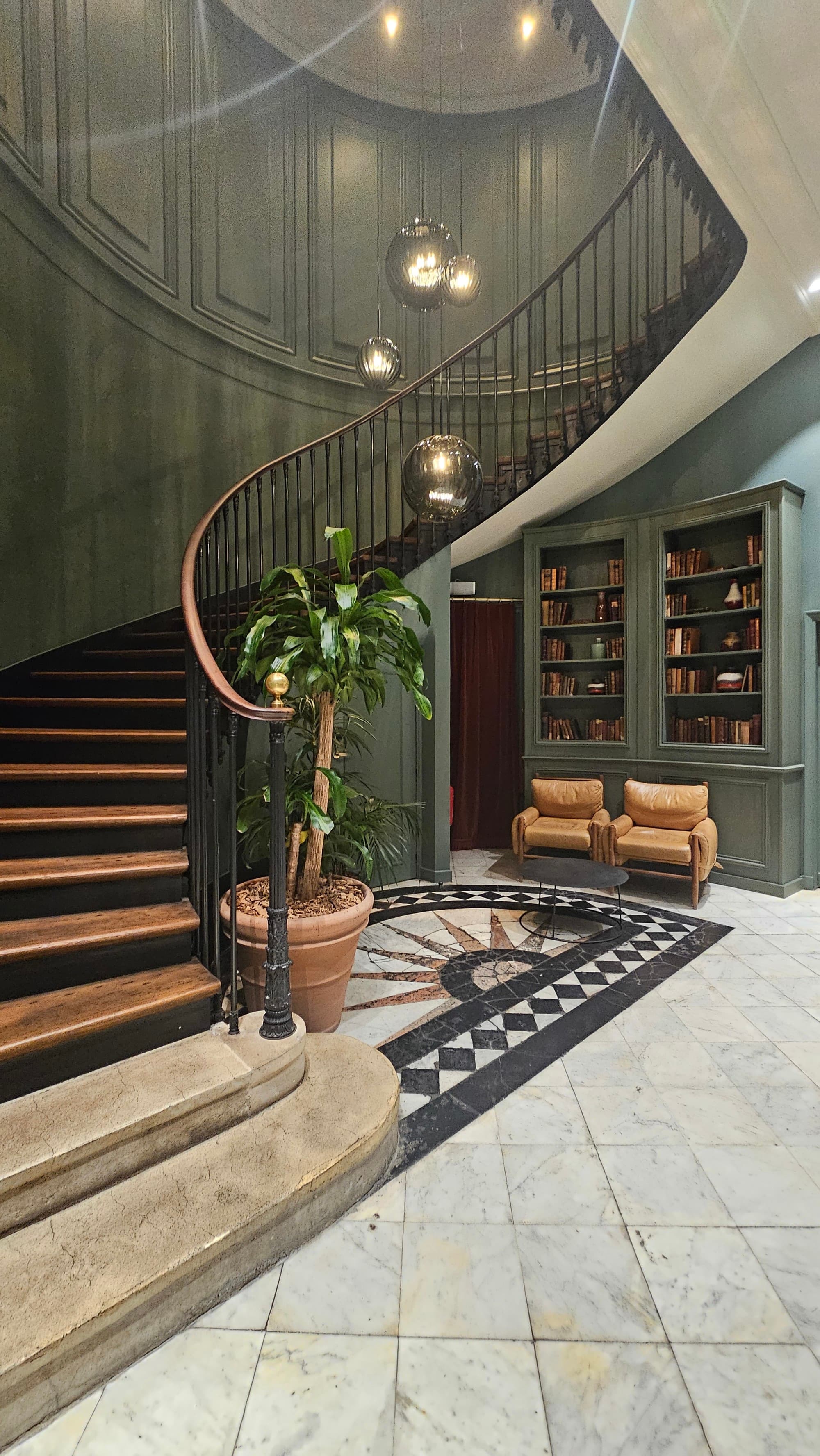 A curved marble staircase leading up from a small lobby area with leather chairs and a bookshelf in one of the best shopping areas in Paris.