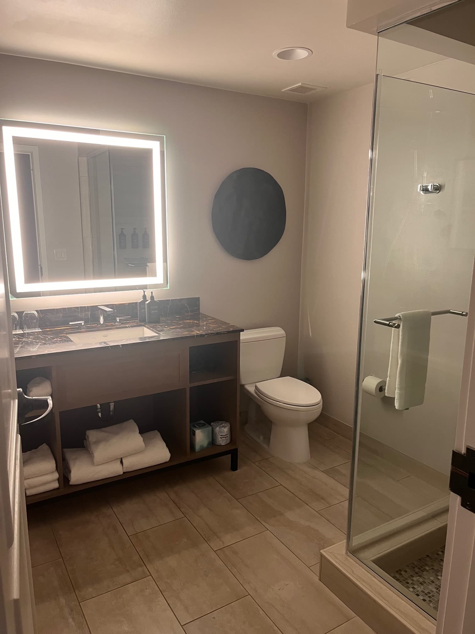 A picture of a hotel bathroom with an illuminated square mirror