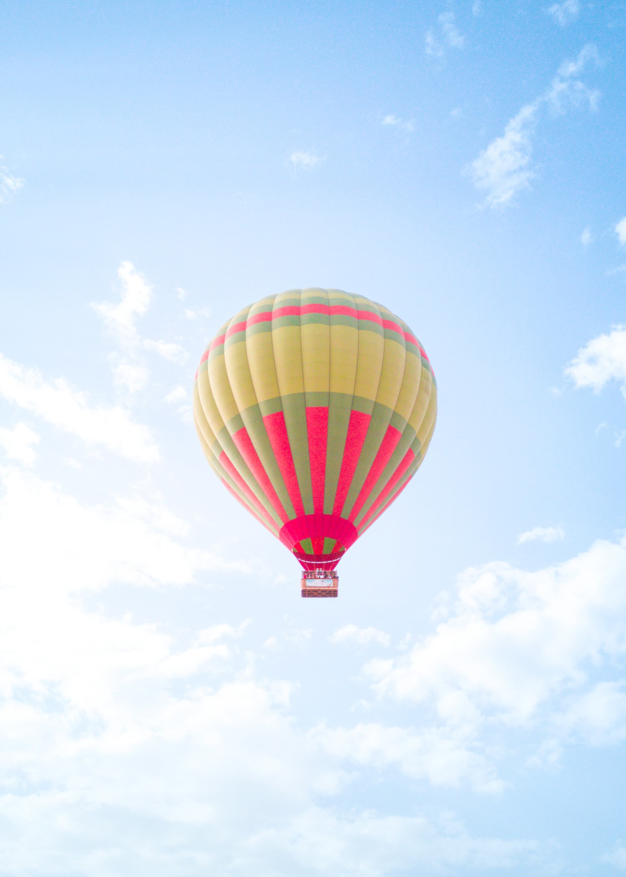 a pink, green, and yellow hot-air balloon in a light-blue sky