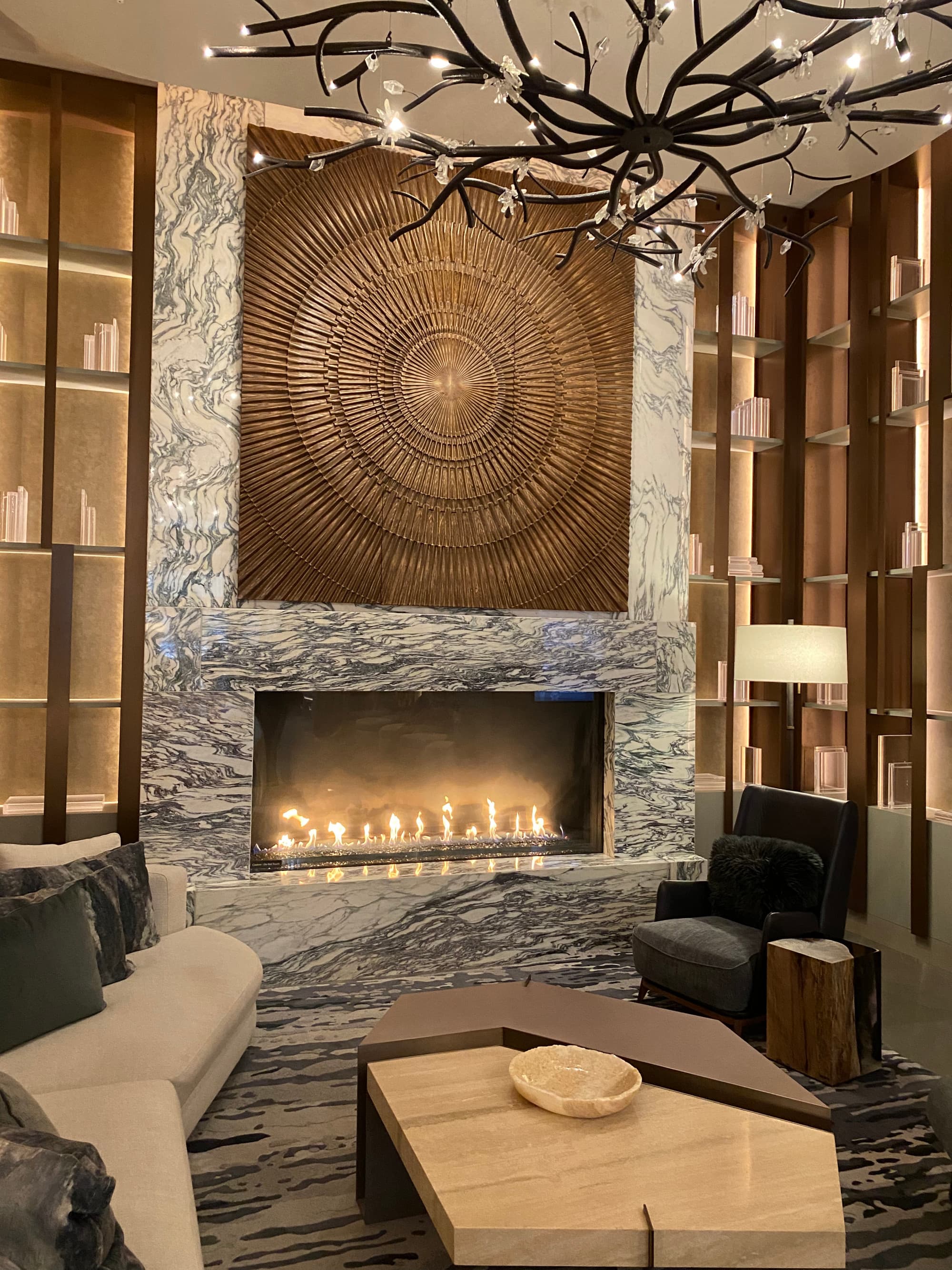 A beautiful hotel lobby with an abstract chandelier, fireplace and golden piece of art on the wall. There are couches and lounge chairs in the space too.