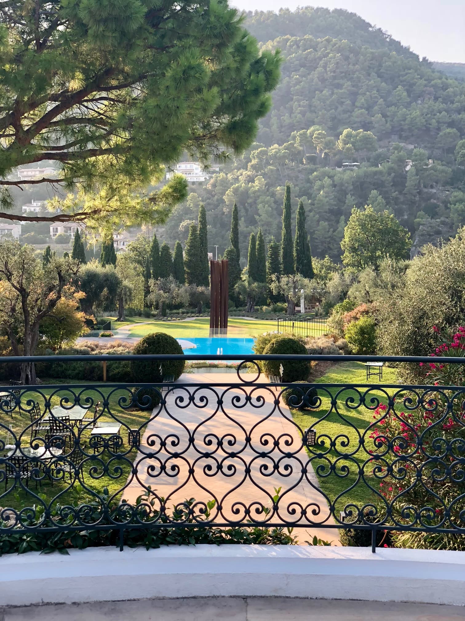 View of the ChateauPool from behind an iron railing on a balcony, with wooded hills in the distance