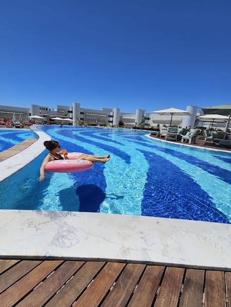 A woman floating on a pink inner tube over the pool with a paneled wood deck in the forefront.