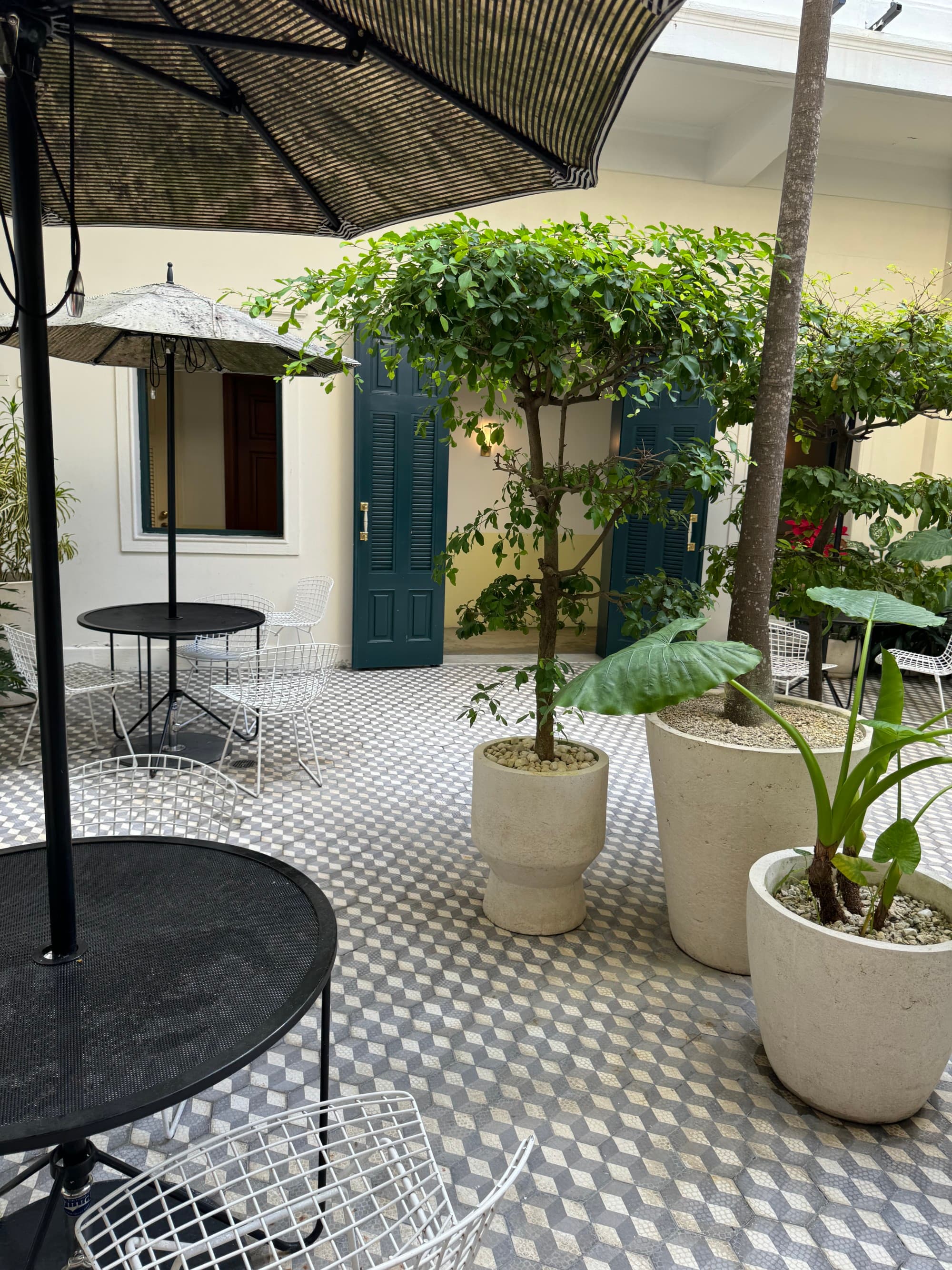 Hotel outside sitting area with potted plants and nice umbrellas for shade on a hot day.