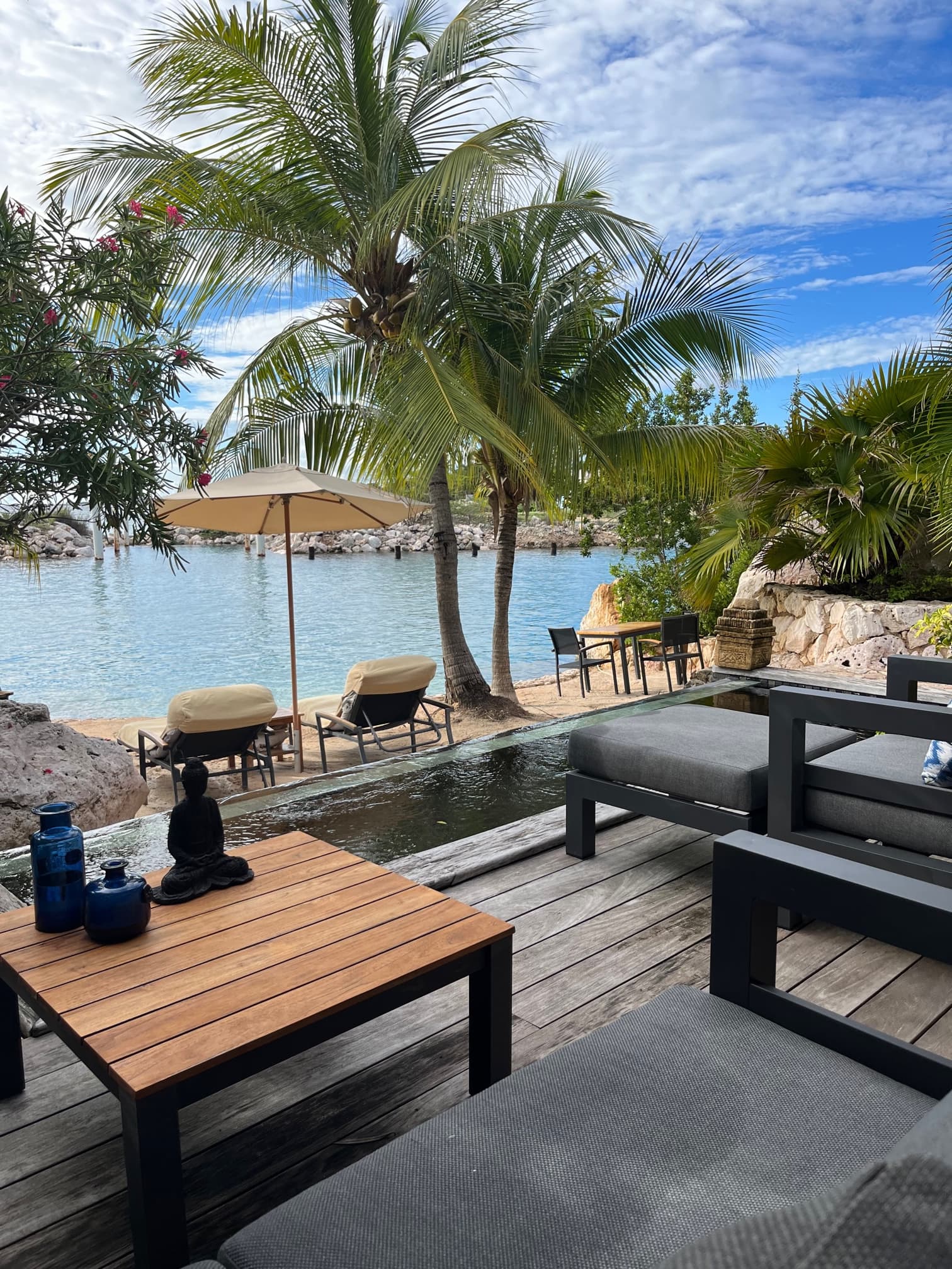 A wooden pool deck looking out onto water with palm trees