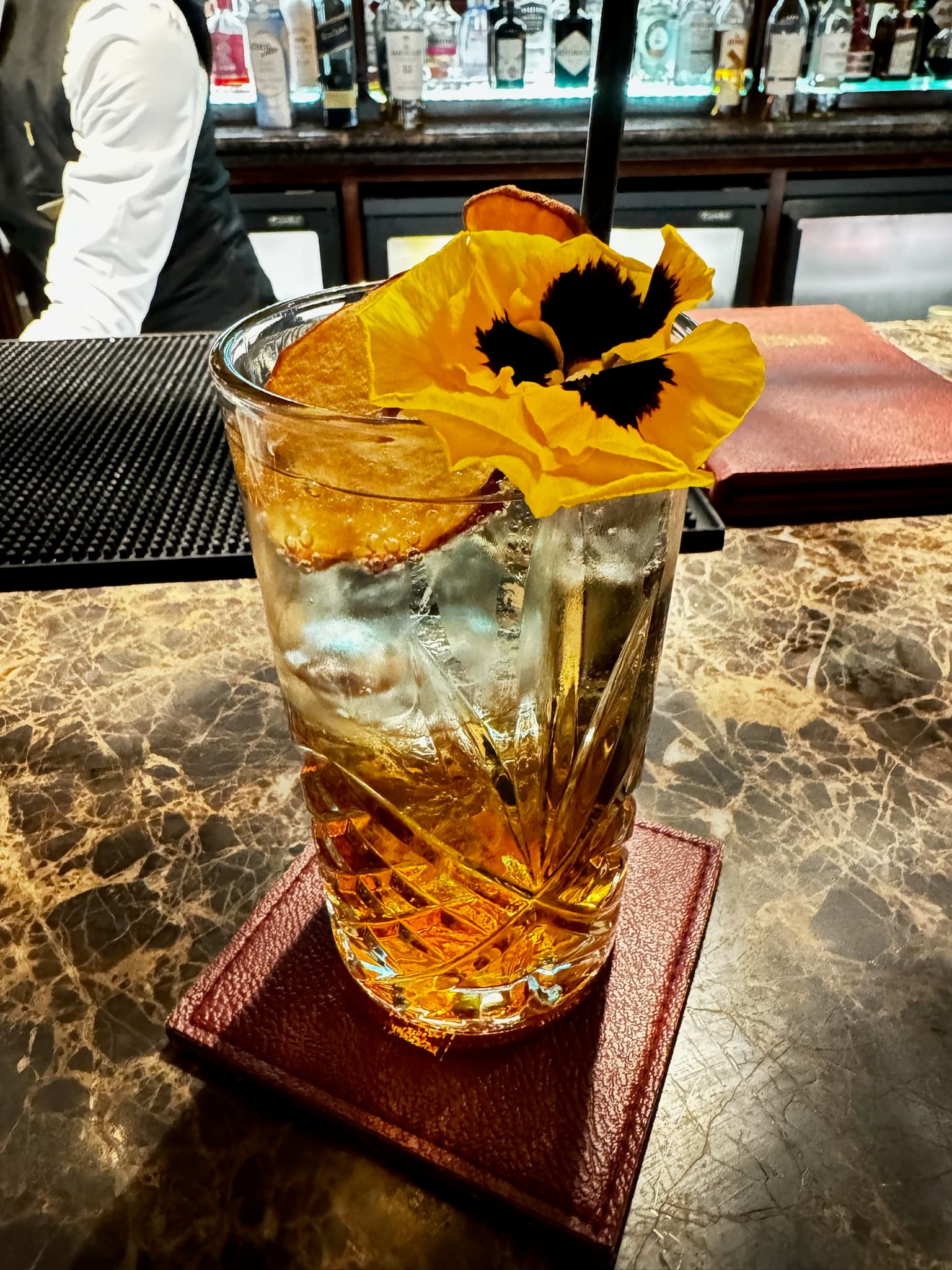 A glistening, crafted cocktail decorated with a yellow flower, atop the hotel's bar.