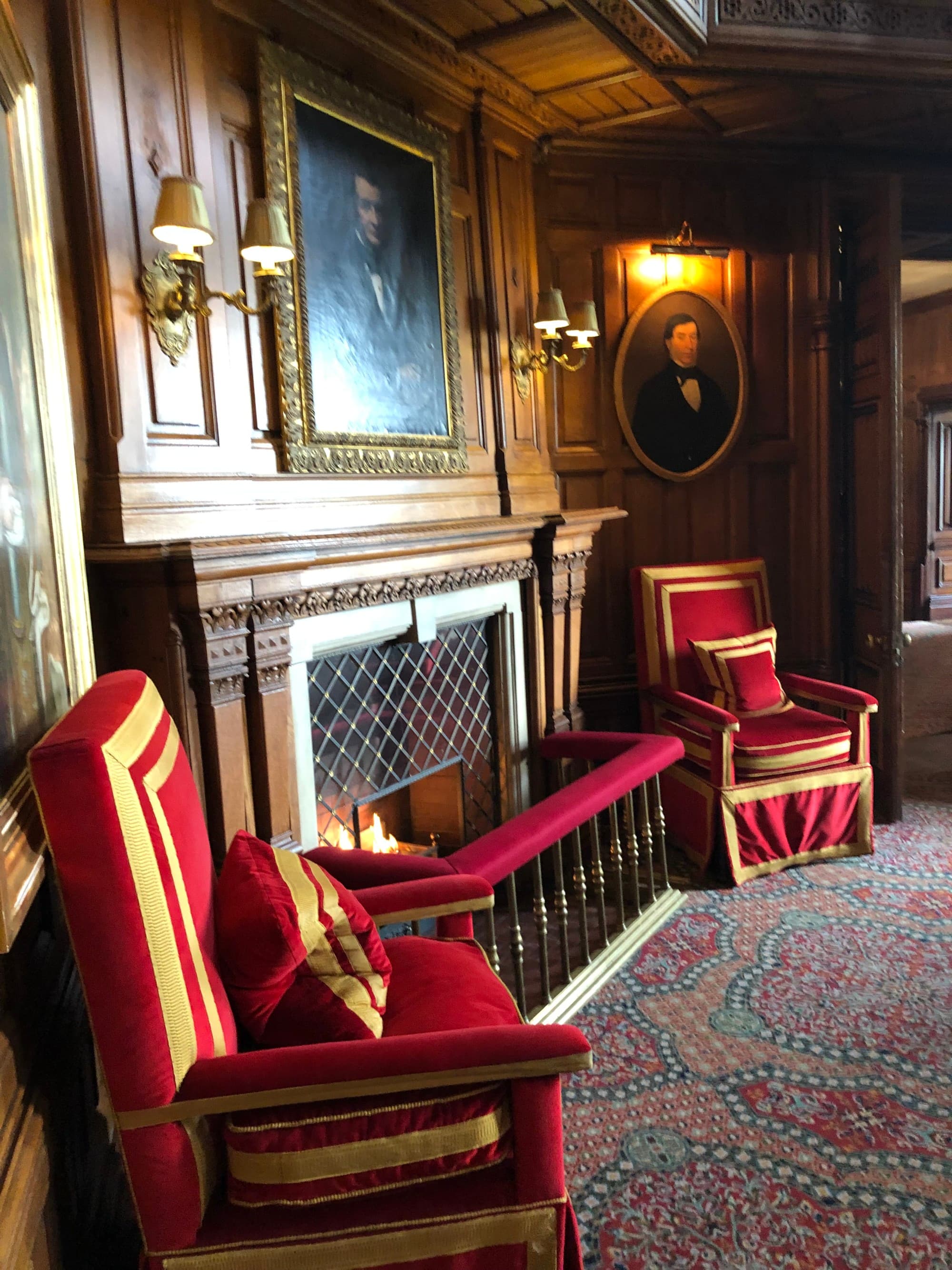 The interior of the hotel with lavish red armchairs and brown paneled walls with antique paintings and a fireplace