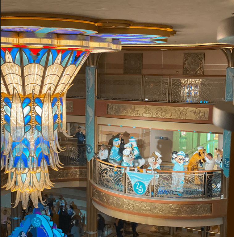 Disney characters dressed up in costumes on a balcony inside the ship, with the peacock light fixture in sight.