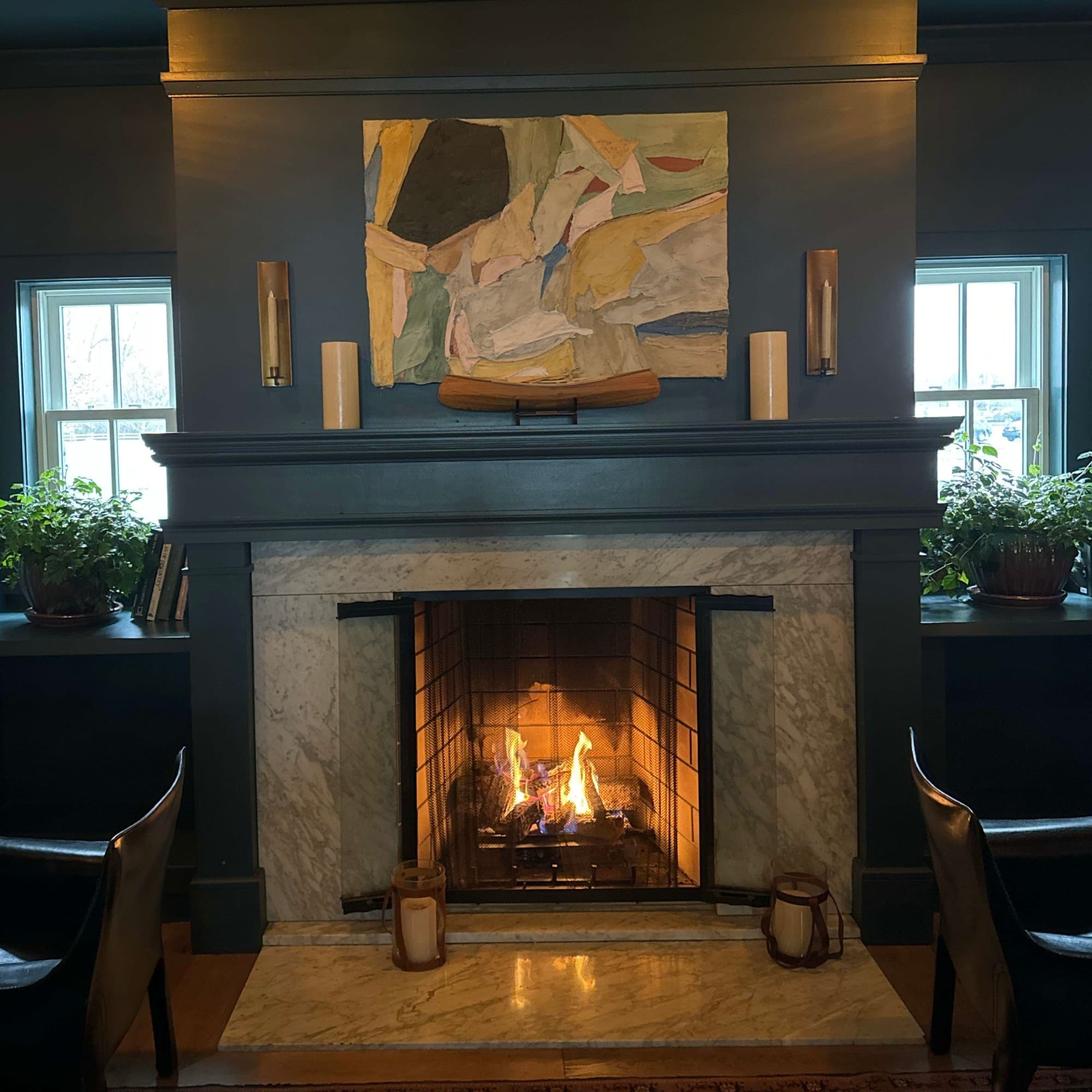 Fireplace with a fire in a hotel lobby with blue walls and leather chairs - Noelle Rudloff