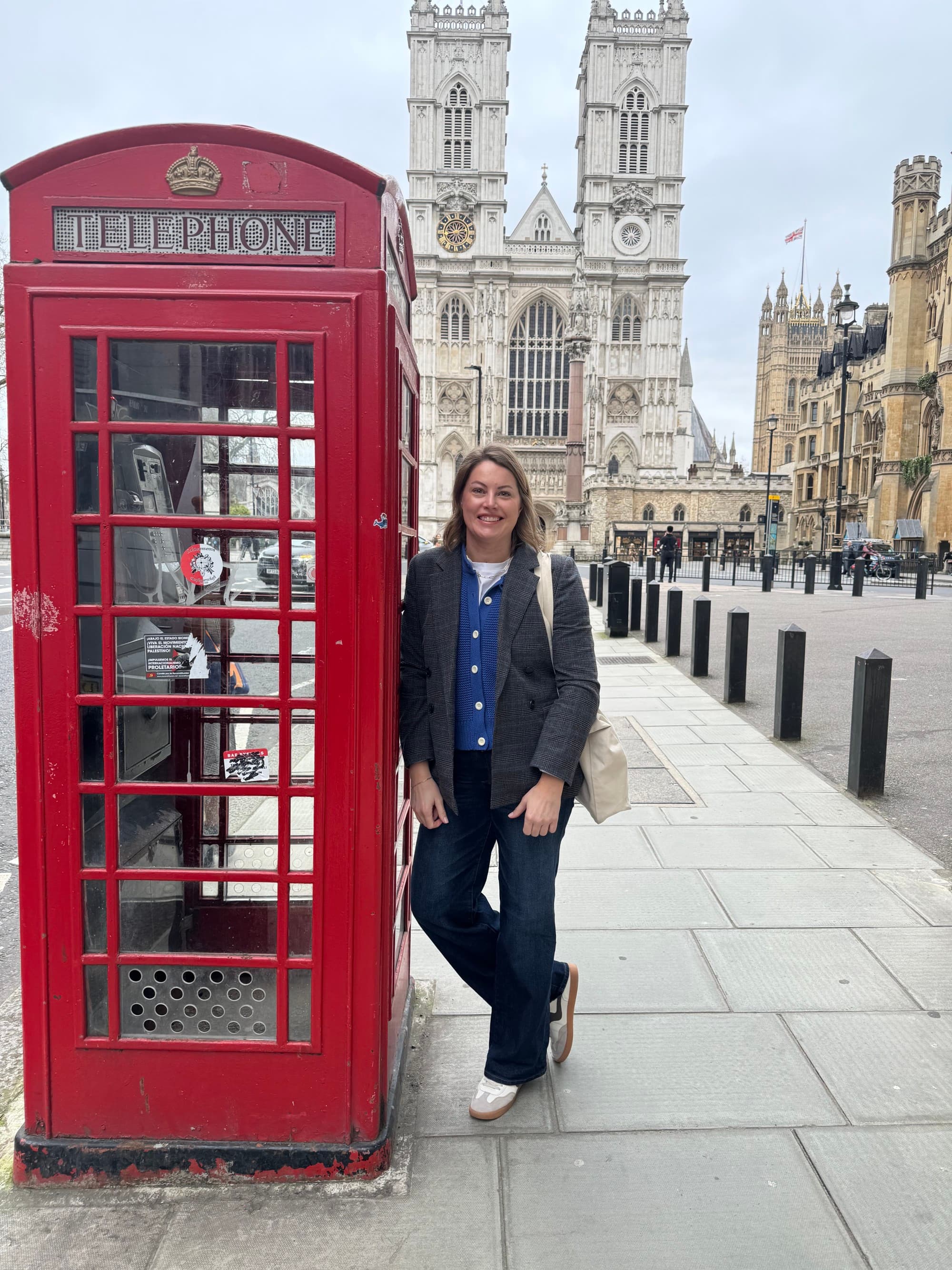 A woman leans against a red phone booth near an old cathedral