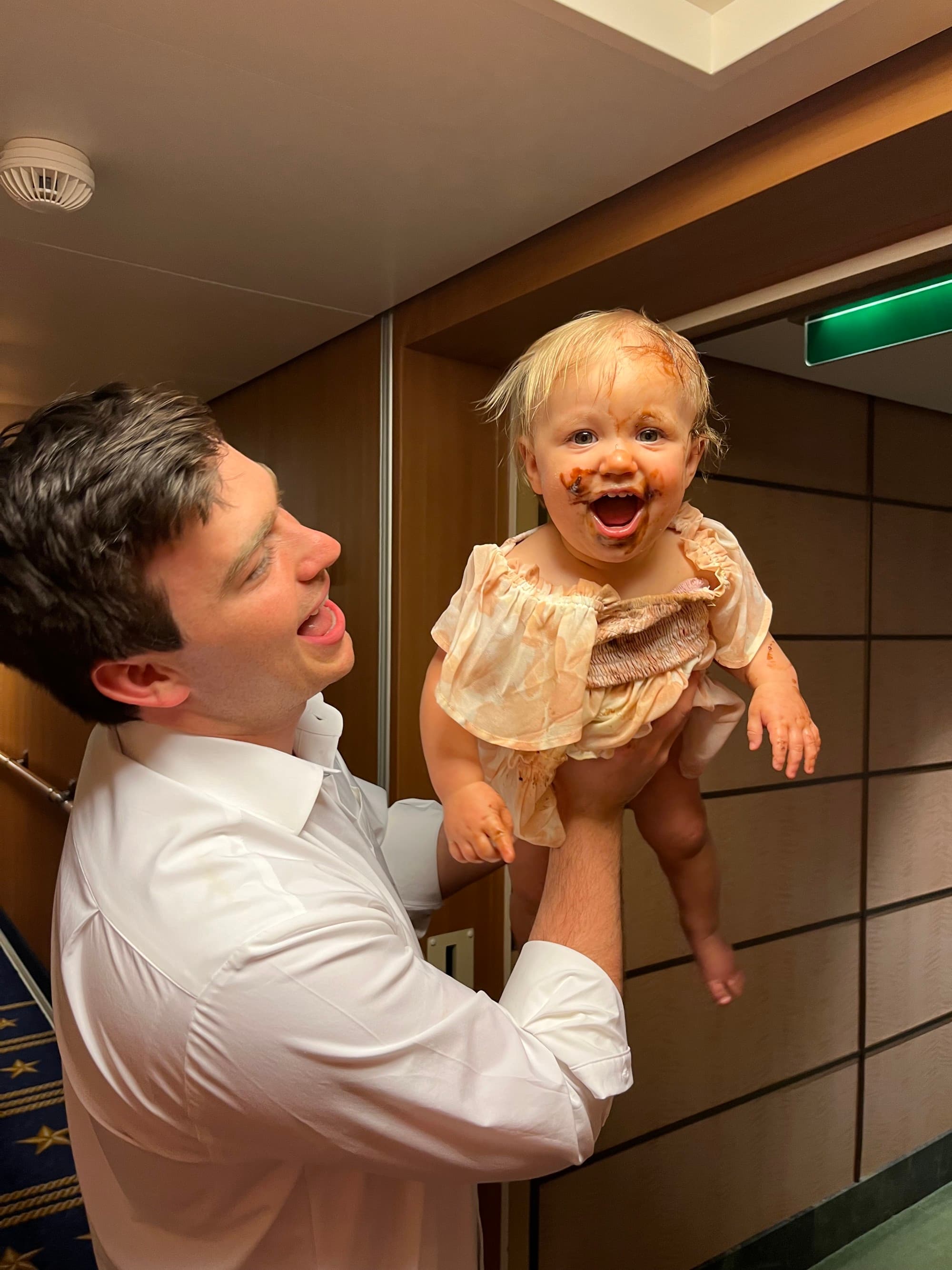 Father holding his baby out, displaying her happy, face full of chocolate.