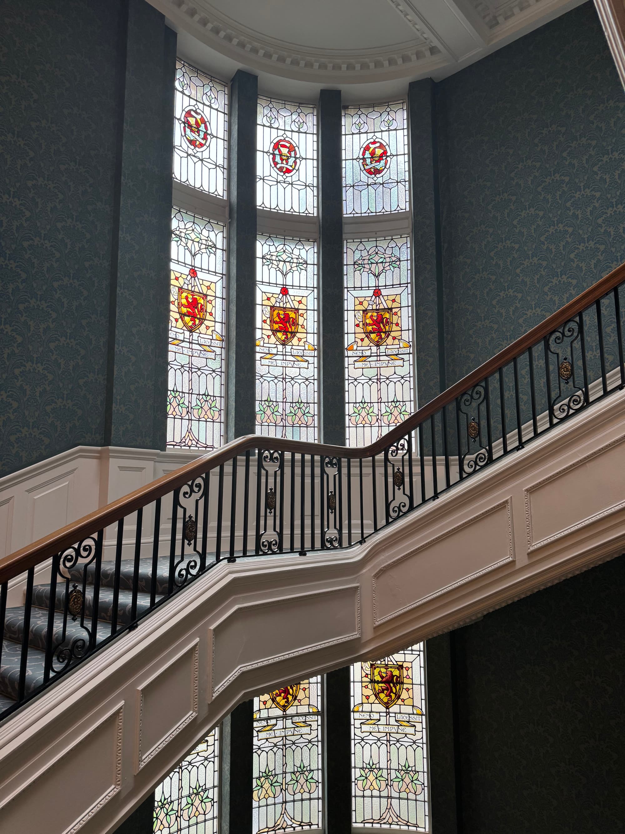 View of a curved staircase inside the hotel with beautiful stained glass windows behind it