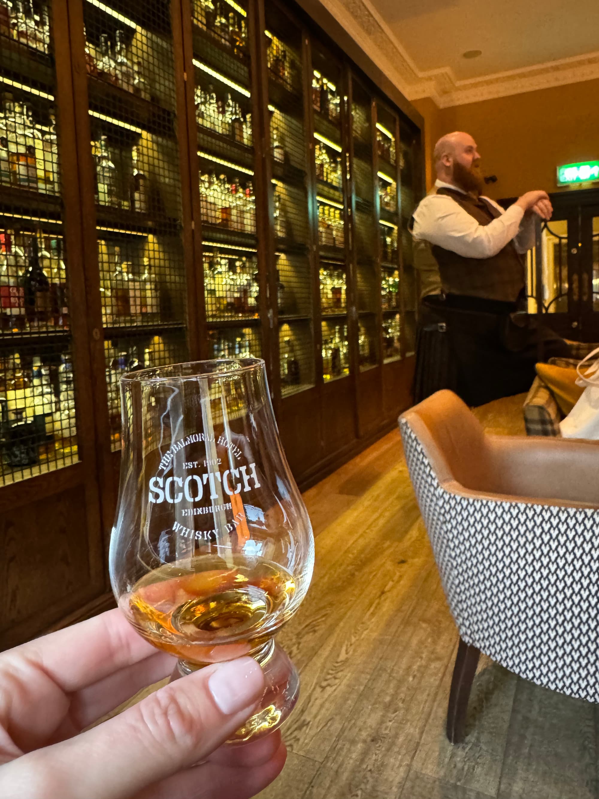 Advisor holding a glass of whisky inside the Balmoral’s whisky bar, an employee seen speaking in the background