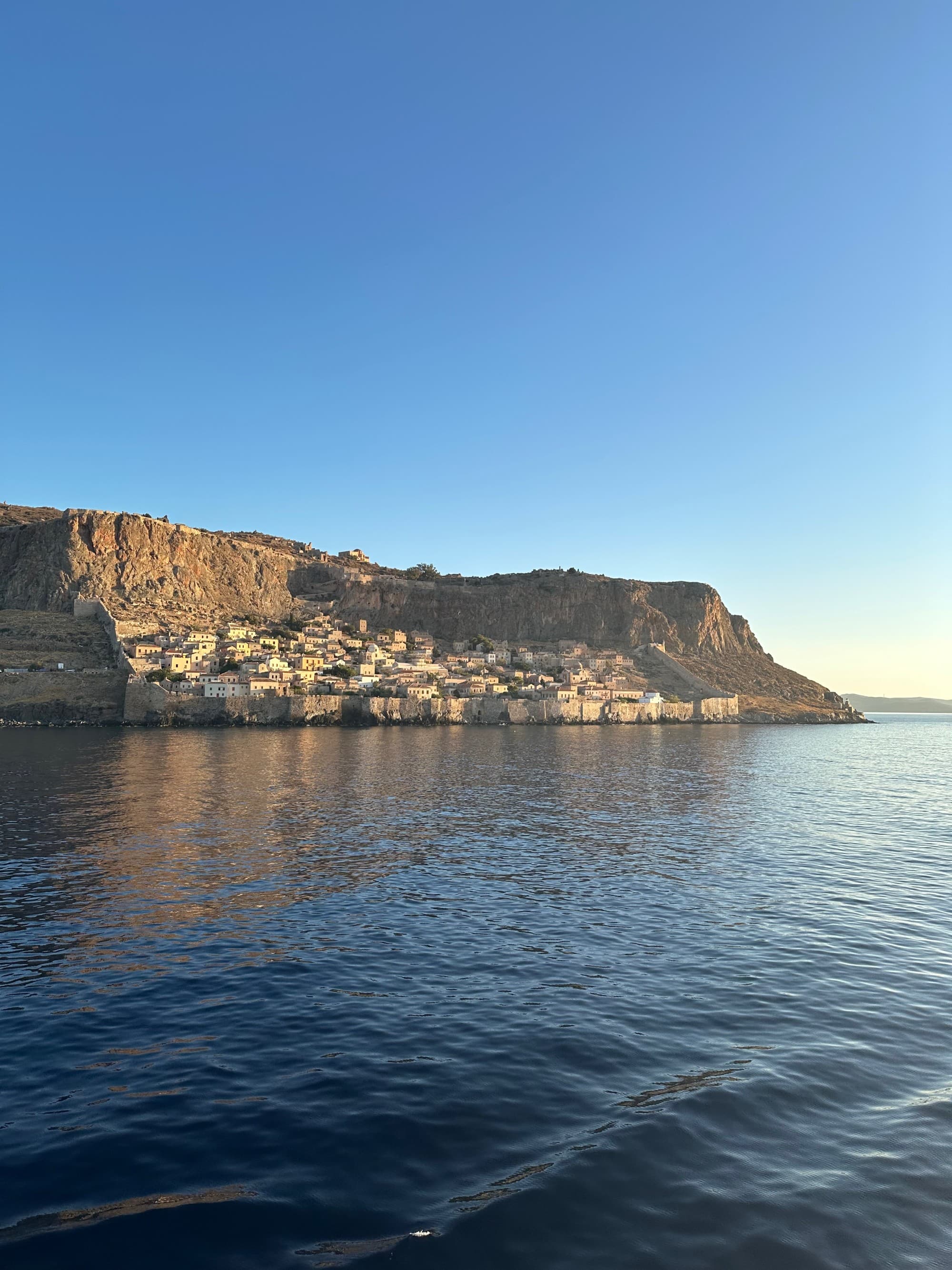 Buildings at the bottom of a cliff on the ocean in Monemvasia - Kristyne Wada